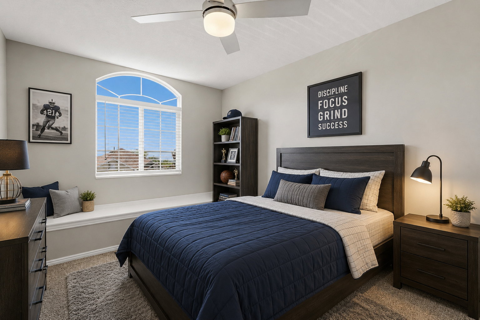 Bedroom featuring an arched window with blinds, a built-in window seat, a ceiling fan, and light gray walls. Staged virtually.