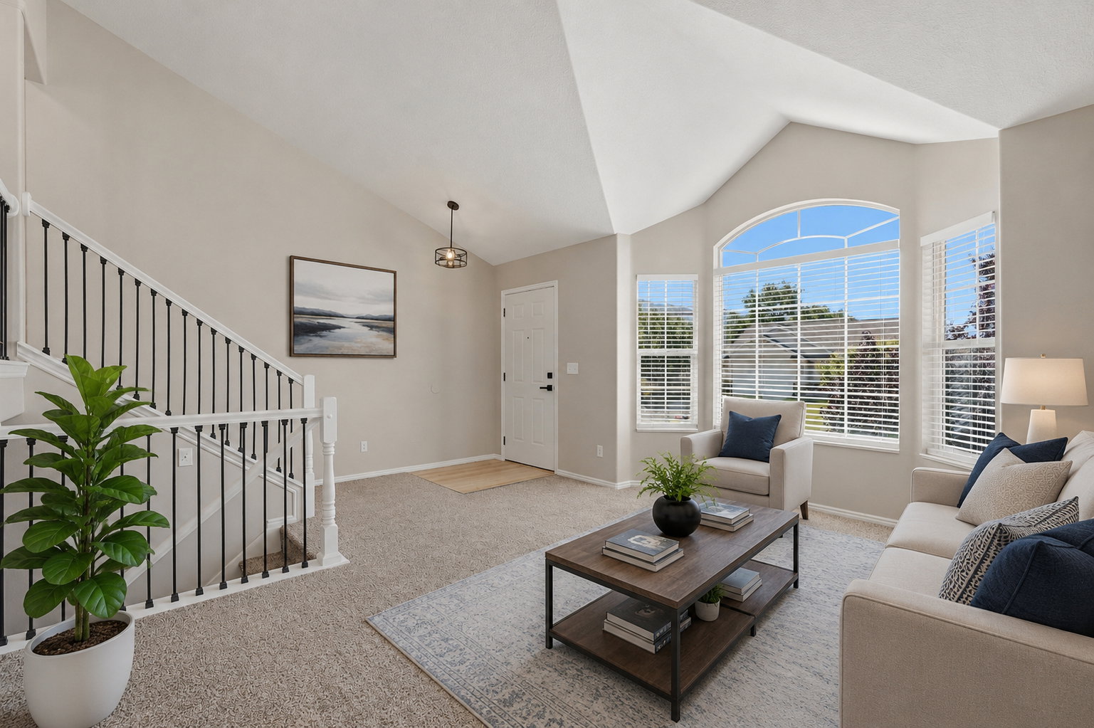 Vaulted ceilings and a large arched window illuminate the living space, featuring neutral carpet and paint throughout. Staged virtually.