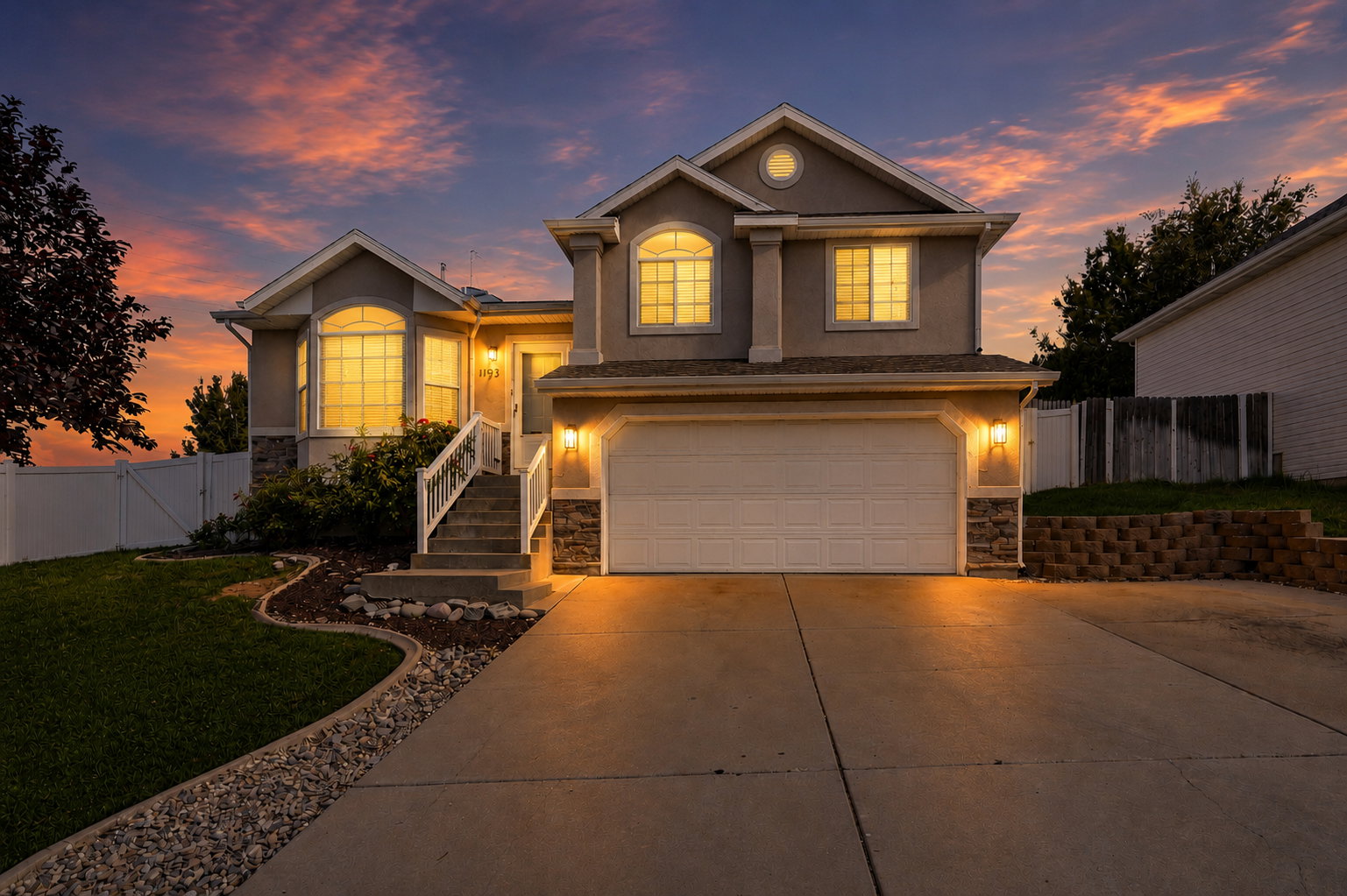 Two-story stucco residence featuring a two-car garage, stone accents, and a concrete driveway. Virtual twilight.