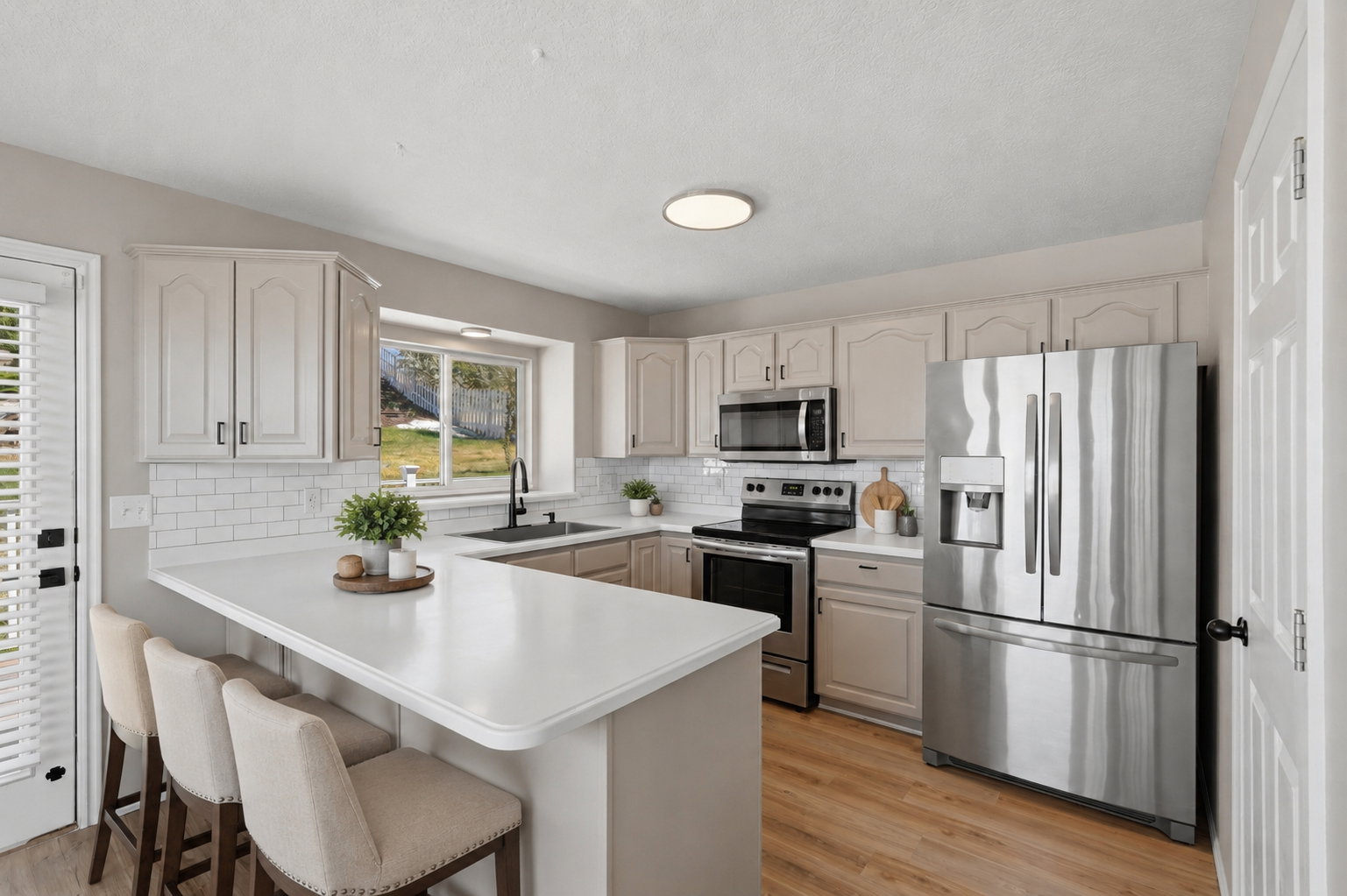 Kitchen featuring a U-shaped countertop with seating, subway tile backsplash, stainless steel appliances, wood-finish flooring, and light-toned cabinetry. Staged virtually.
