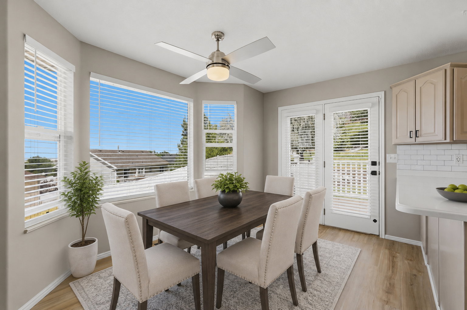 Dining area featuring a bay window, wood-finish flooring, and a ceiling fan with light fixture. Staged virtually.