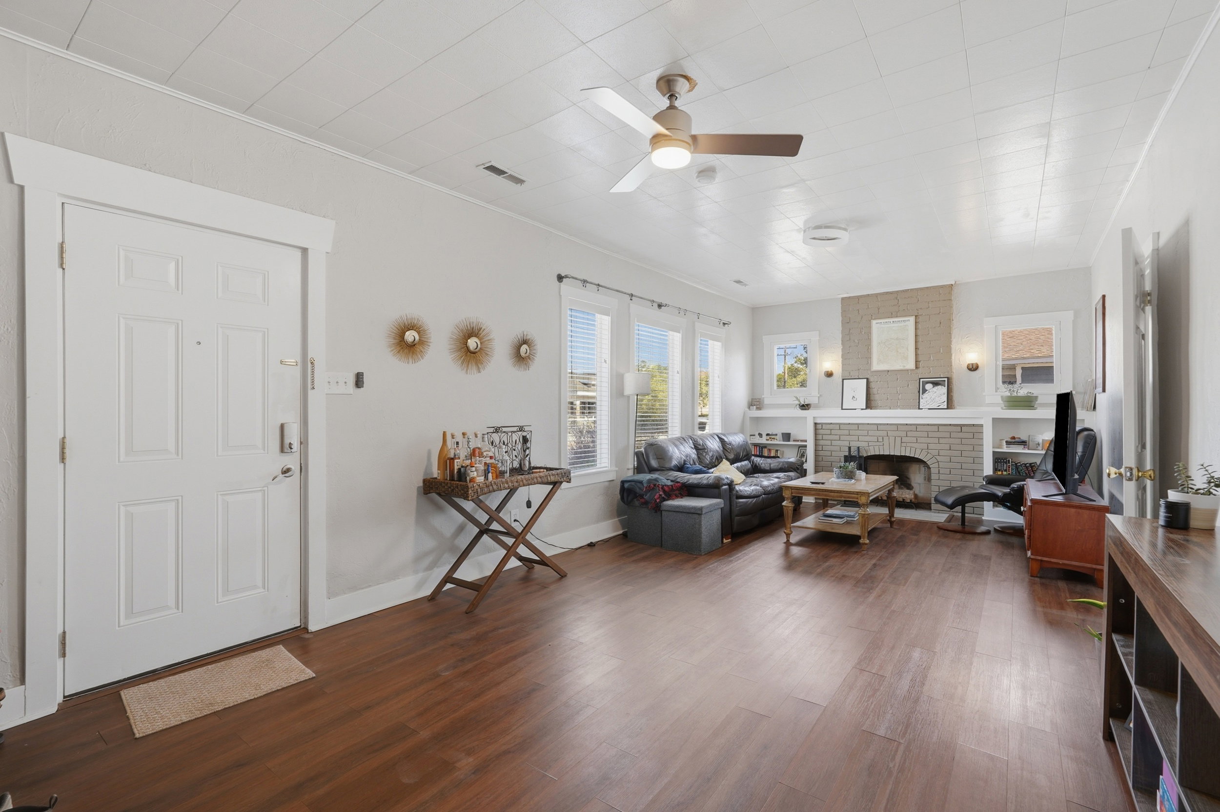 Open living area featuring wood-finish flooring, a ceiling fan, and multiple windows