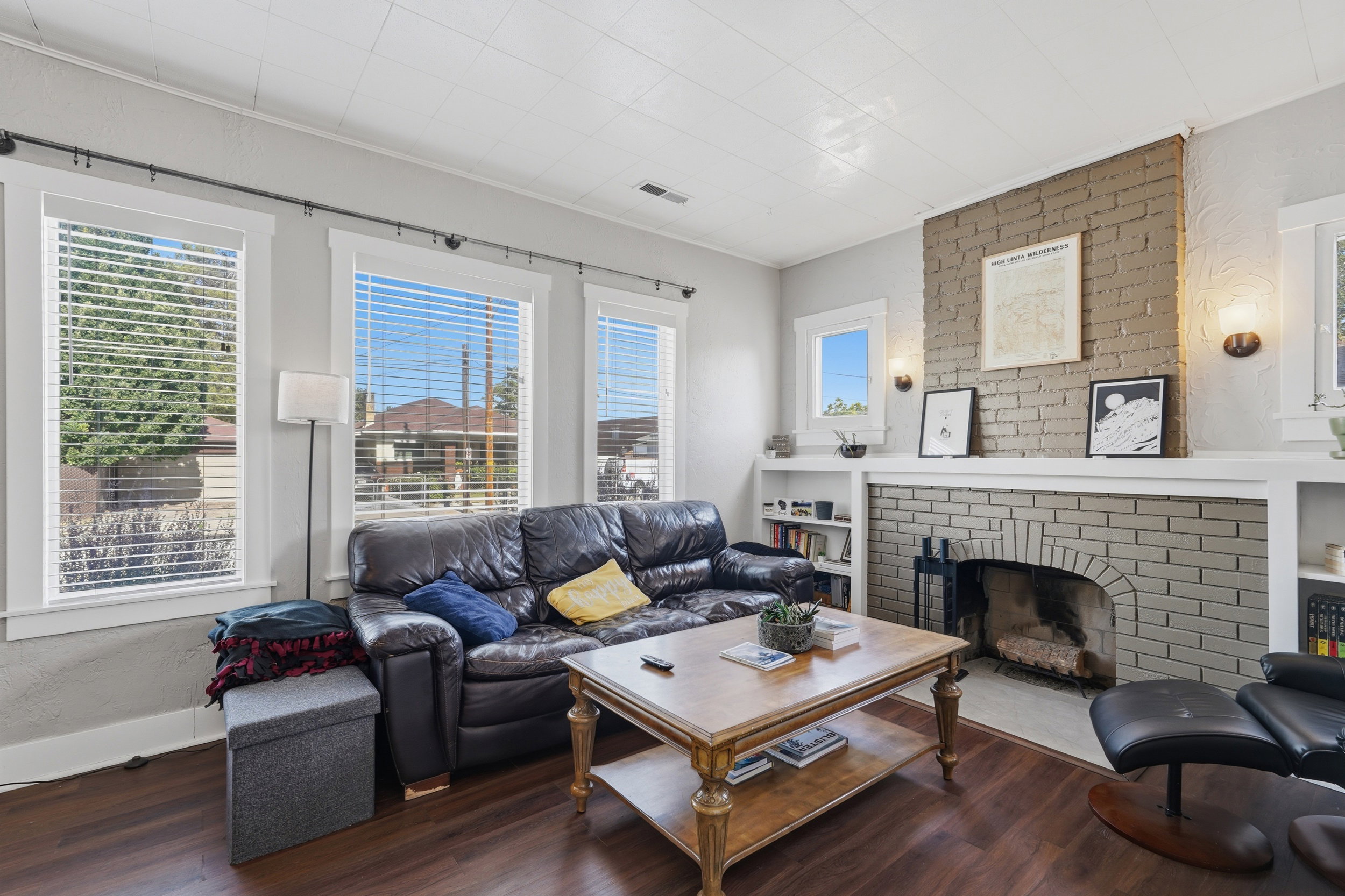 Living space featuring dark wood-finish flooring, multiple windows with blinds, and a brick-surround fireplace with hearth