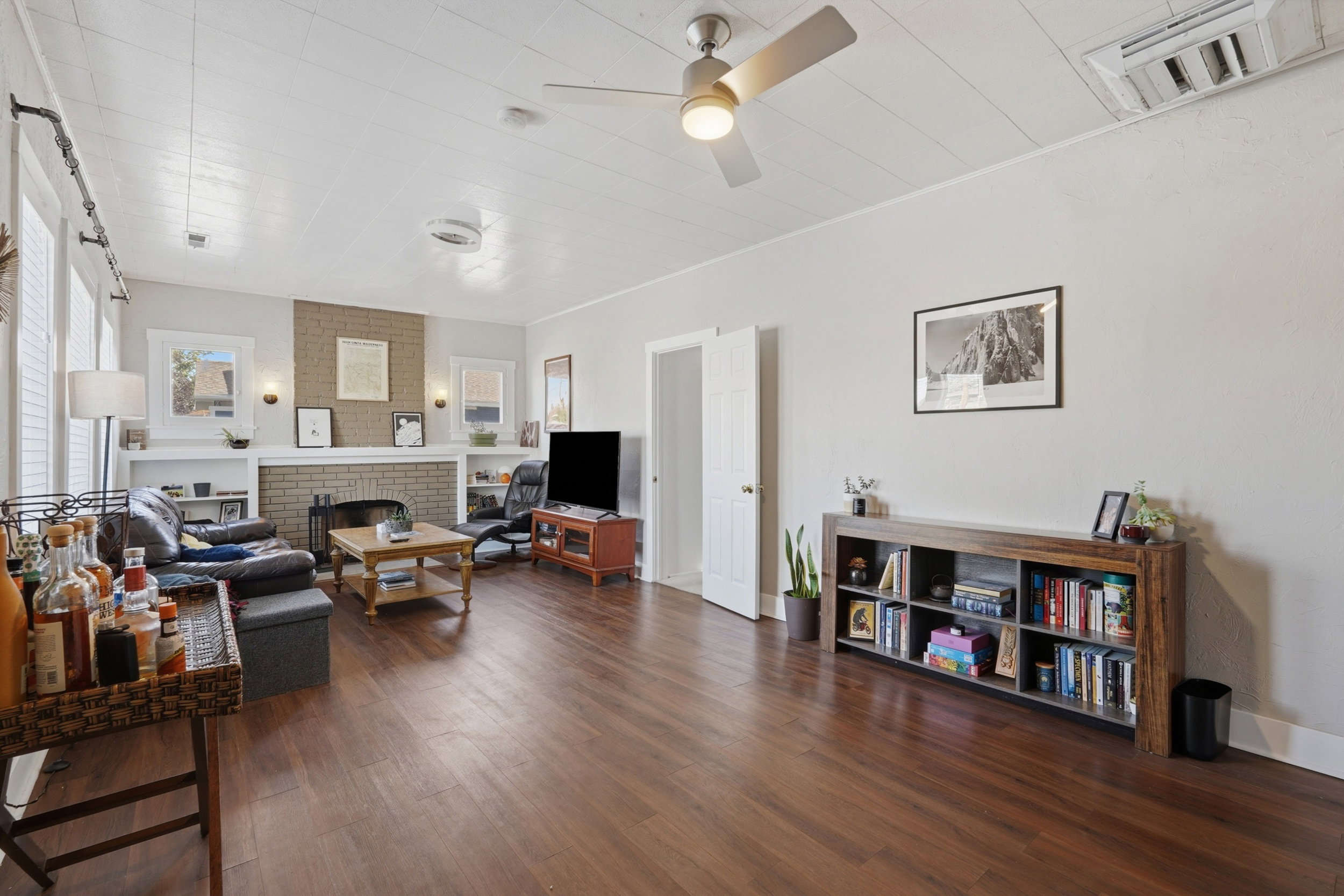 Spacious interior room featuring wood-finish flooring, a brick fireplace with a white mantel, and built-in shelving