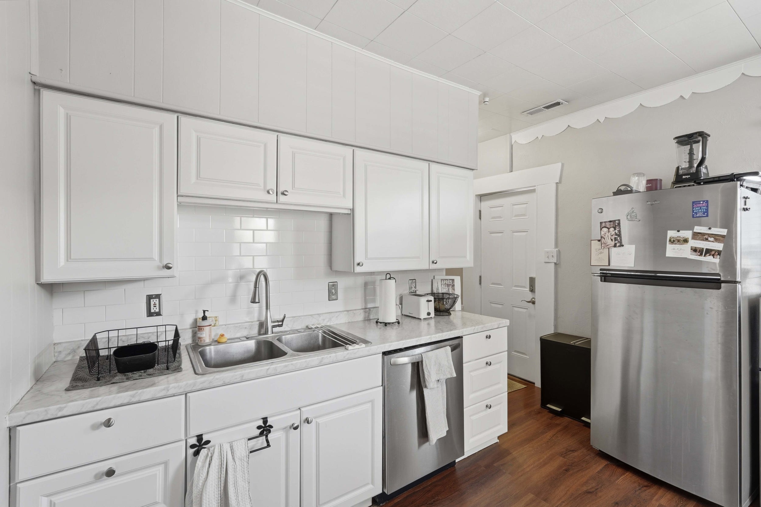 Kitchen featuring white shaker-style cabinetry, a white subway tile backsplash, and a double basin stainless steel sink with a high-arc faucet