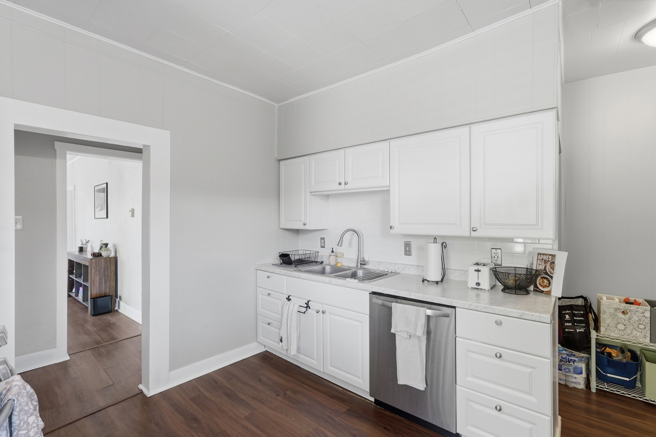 Kitchen featuring white cabinetry, stainless steel dishwasher, double basin sink, white subway tile backsplash, and wood-finish flooring