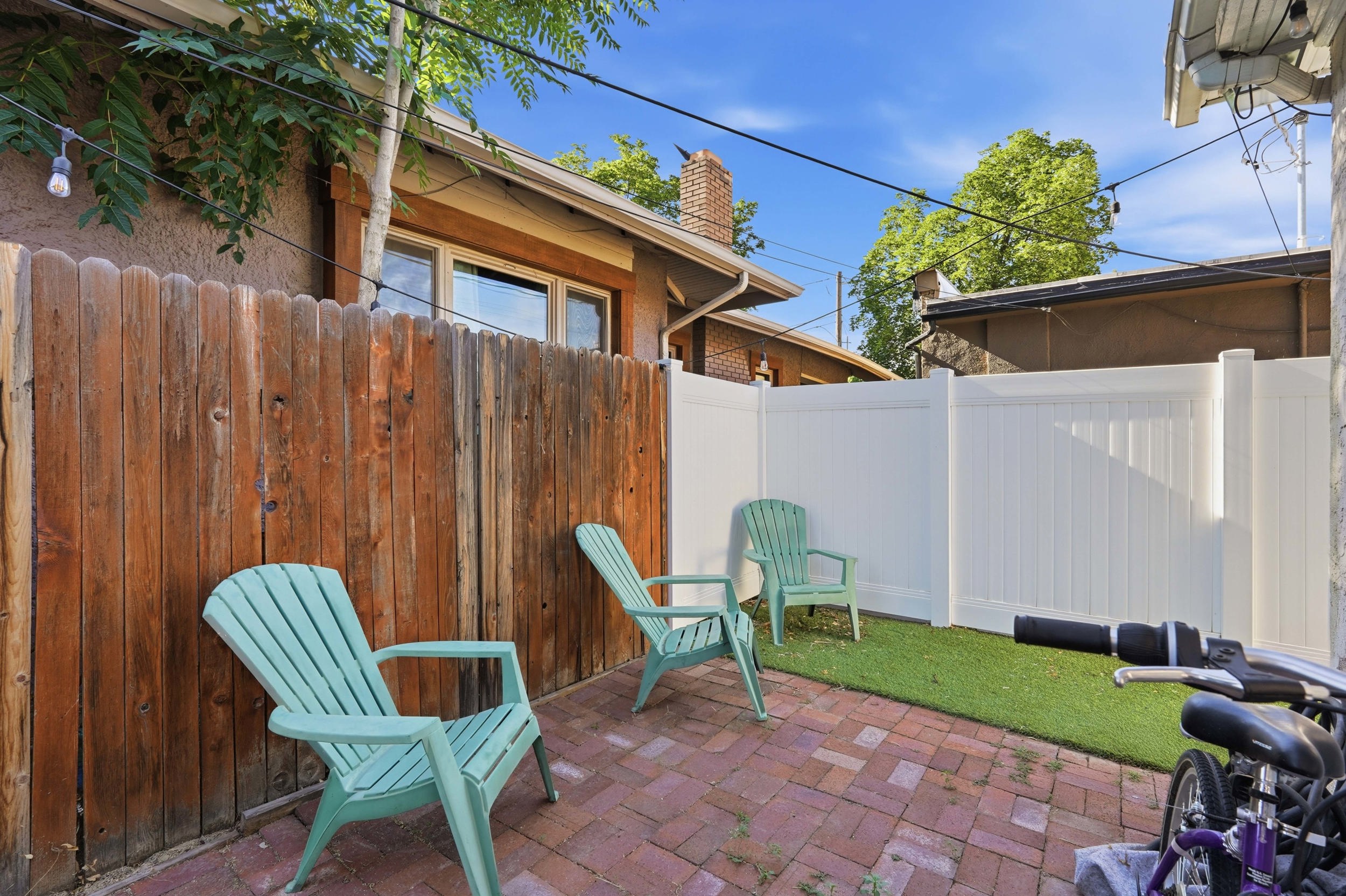 Private outdoor patio featuring brick paver flooring, artificial turf, and wood fencing