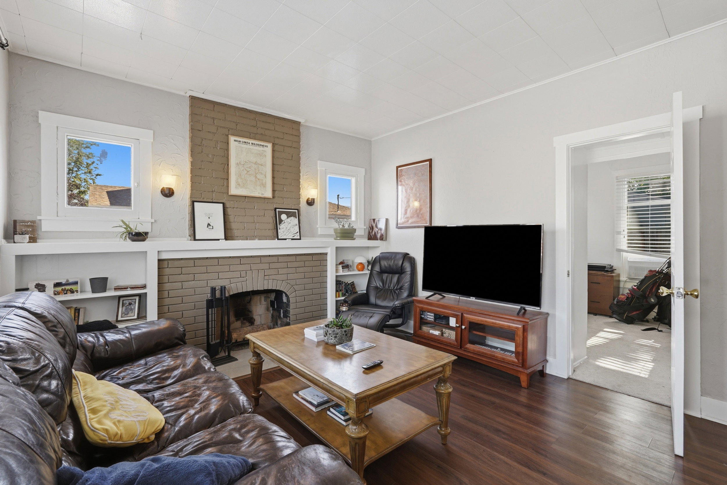 Living area featuring a brick fireplace, built-in shelving, sconce lighting, wood-finish flooring, and white trim