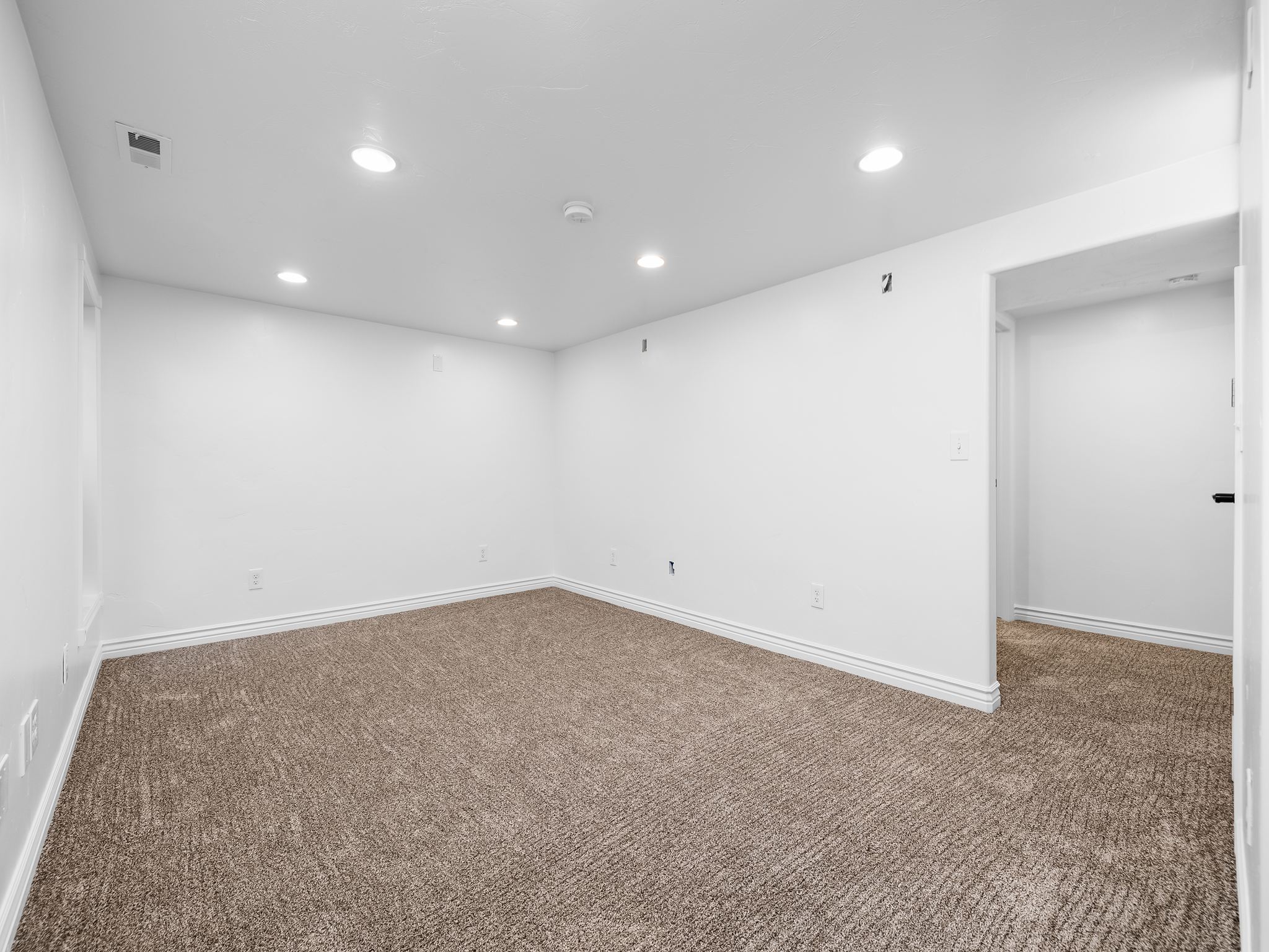 Spacious room featuring neutral-toned carpet flooring, crisp white walls, recessed ceiling lighting, and white baseboards