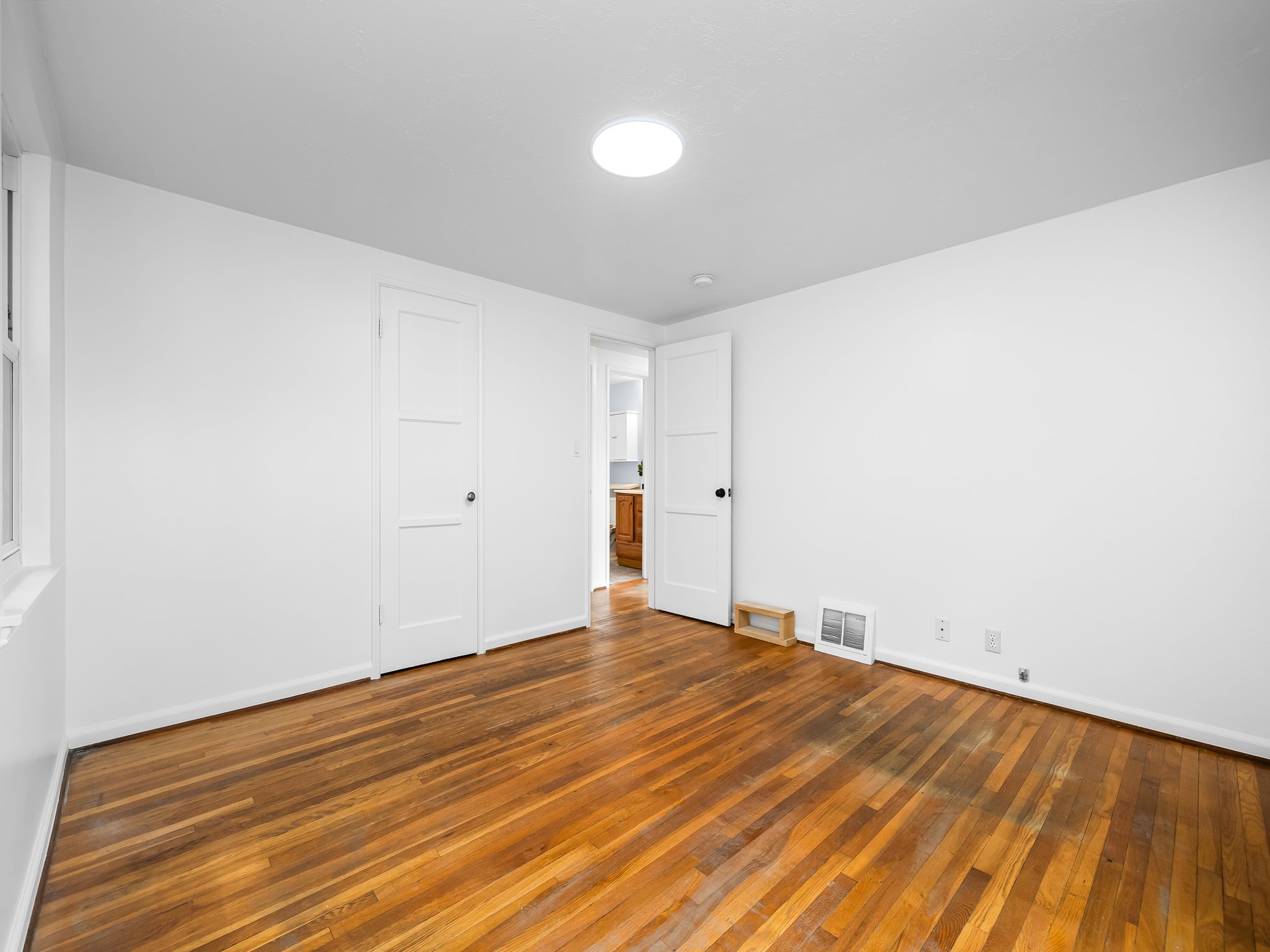 Hardwood flooring throughout, featuring crisp white walls, a flush-mount ceiling light, and white trim