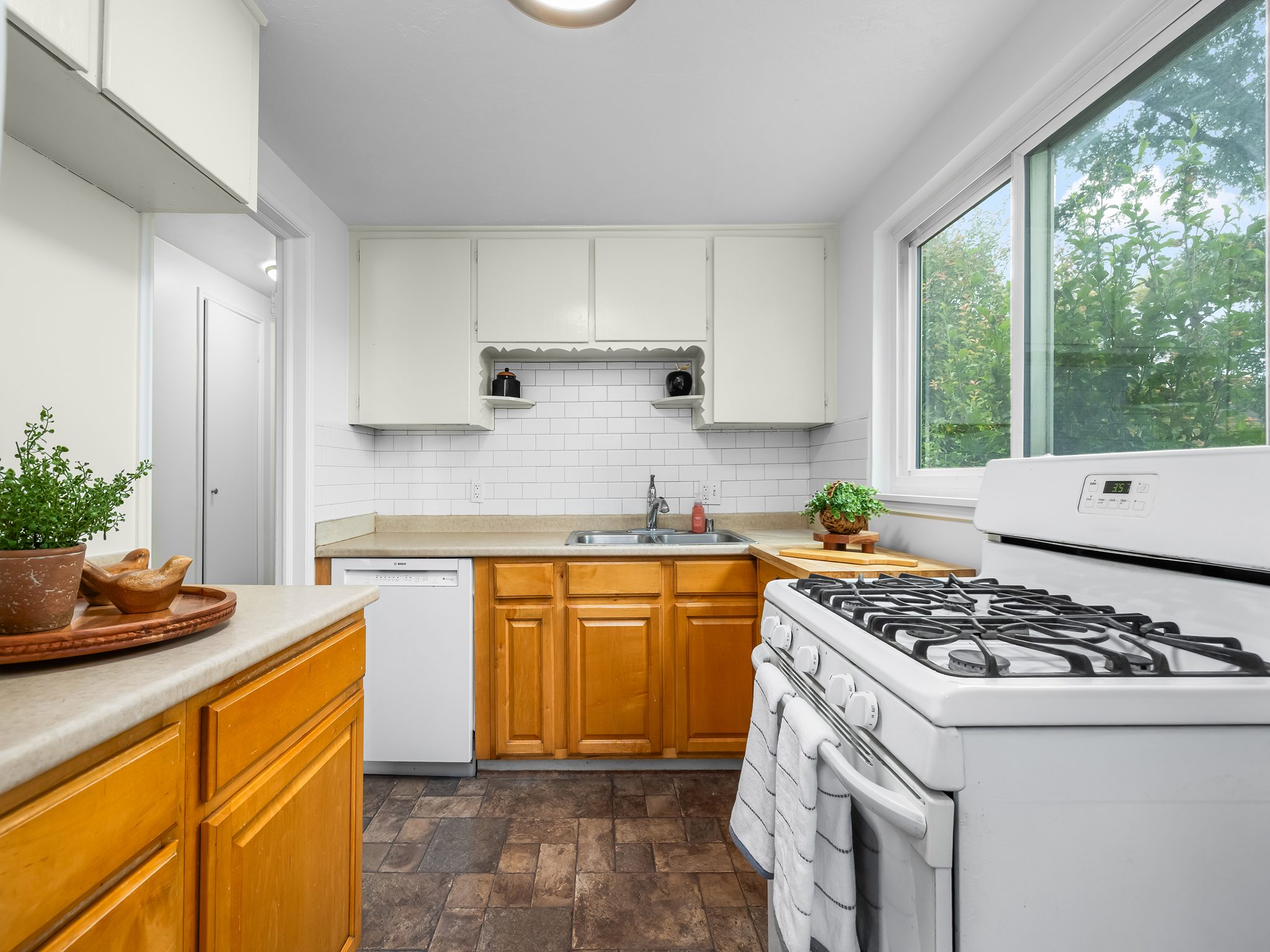 Kitchen featuring a full-size window, white subway tile backsplash, white upper cabinetry, natural wood lower cabinetry, and a gas range
