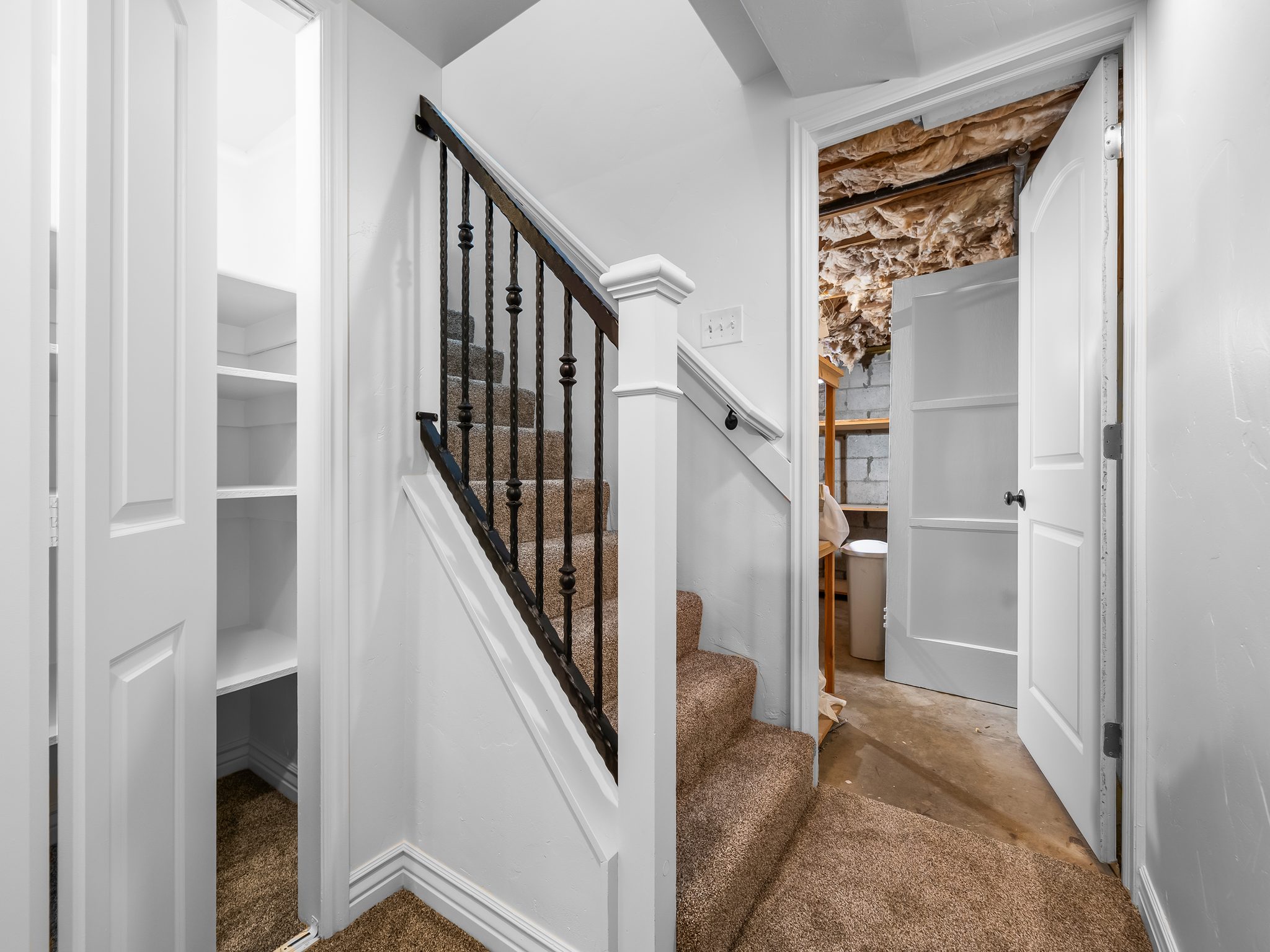 Carpeted staircase with black wrought iron balusters and white newel post