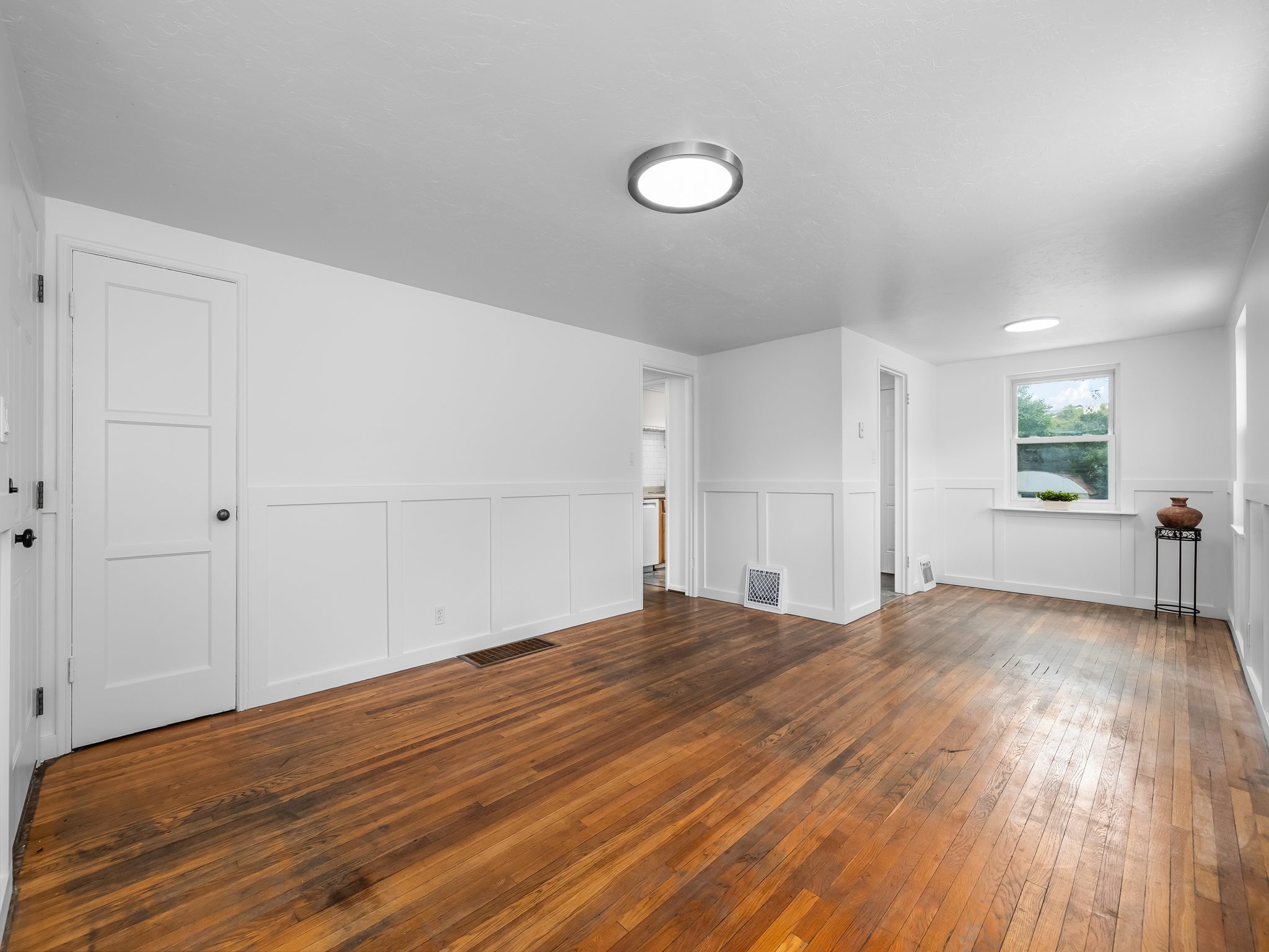Spacious room featuring wood-finish flooring, white paneled wainscoting, and white walls