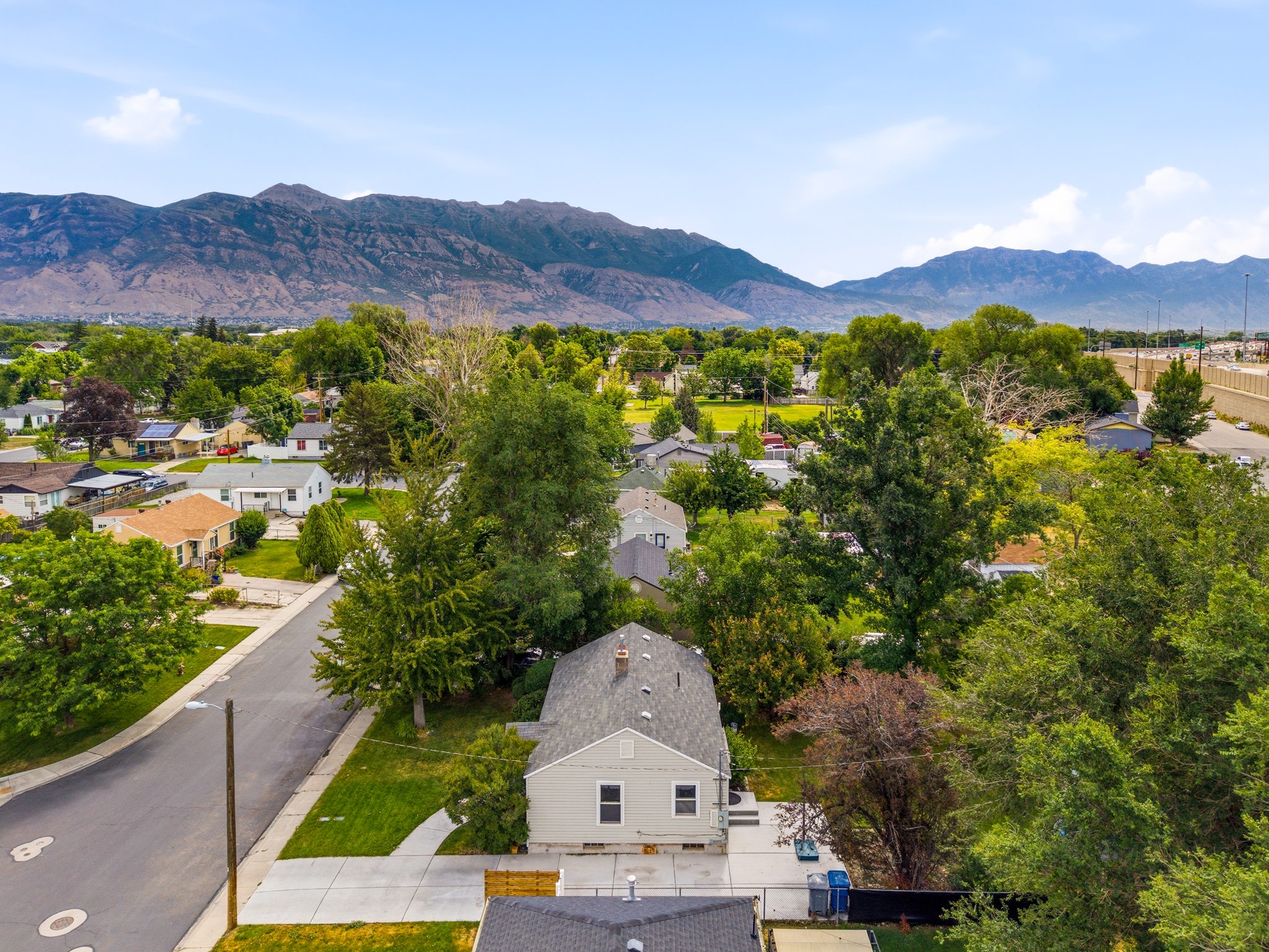 Aerial perspective showcasing a light-colored residential structure with a gray shingle roof, positioned on a street with mature trees