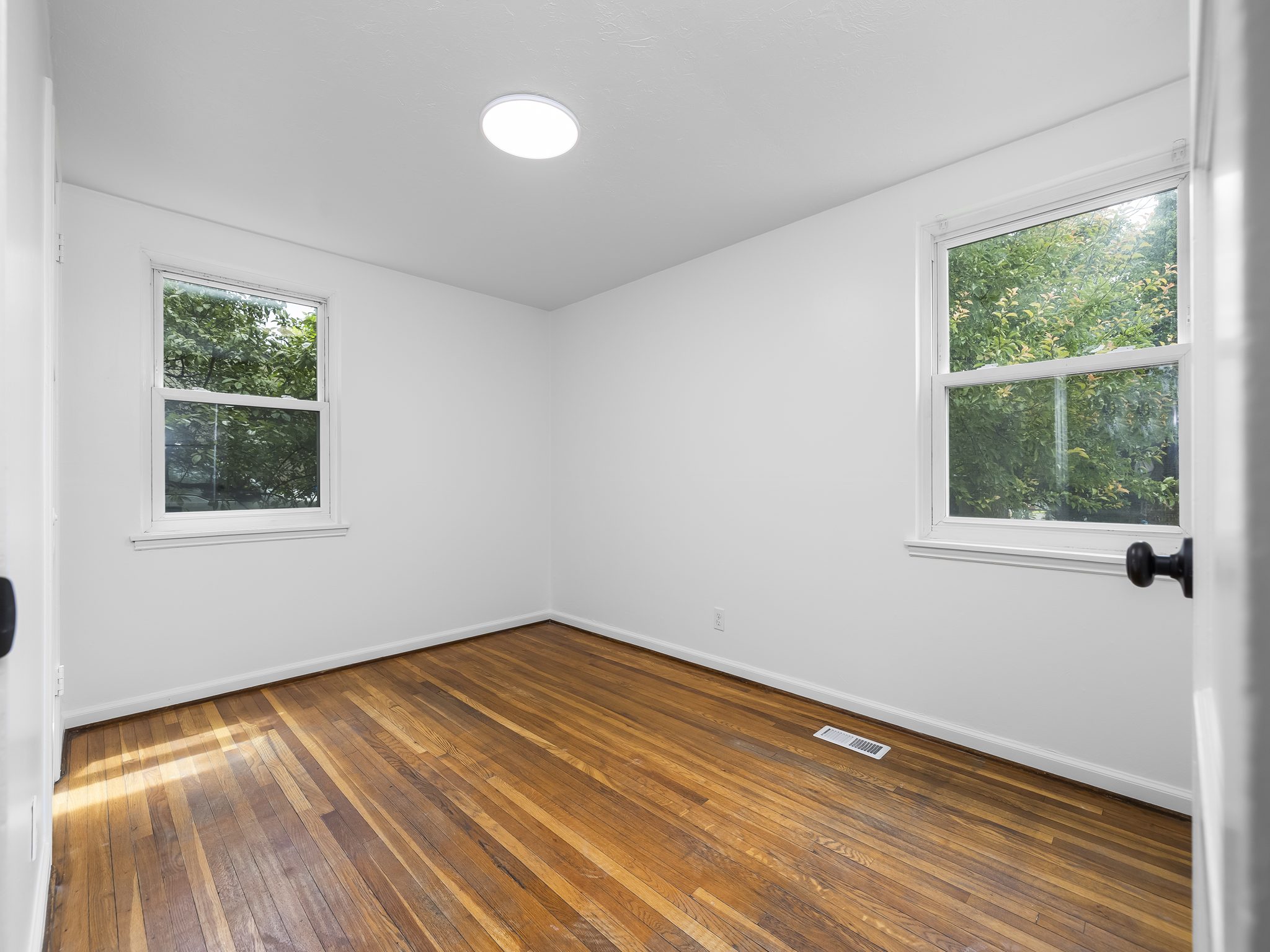 Bright interior space featuring wood-finish flooring, two windows with white trim, and a flush-mount ceiling light fixture