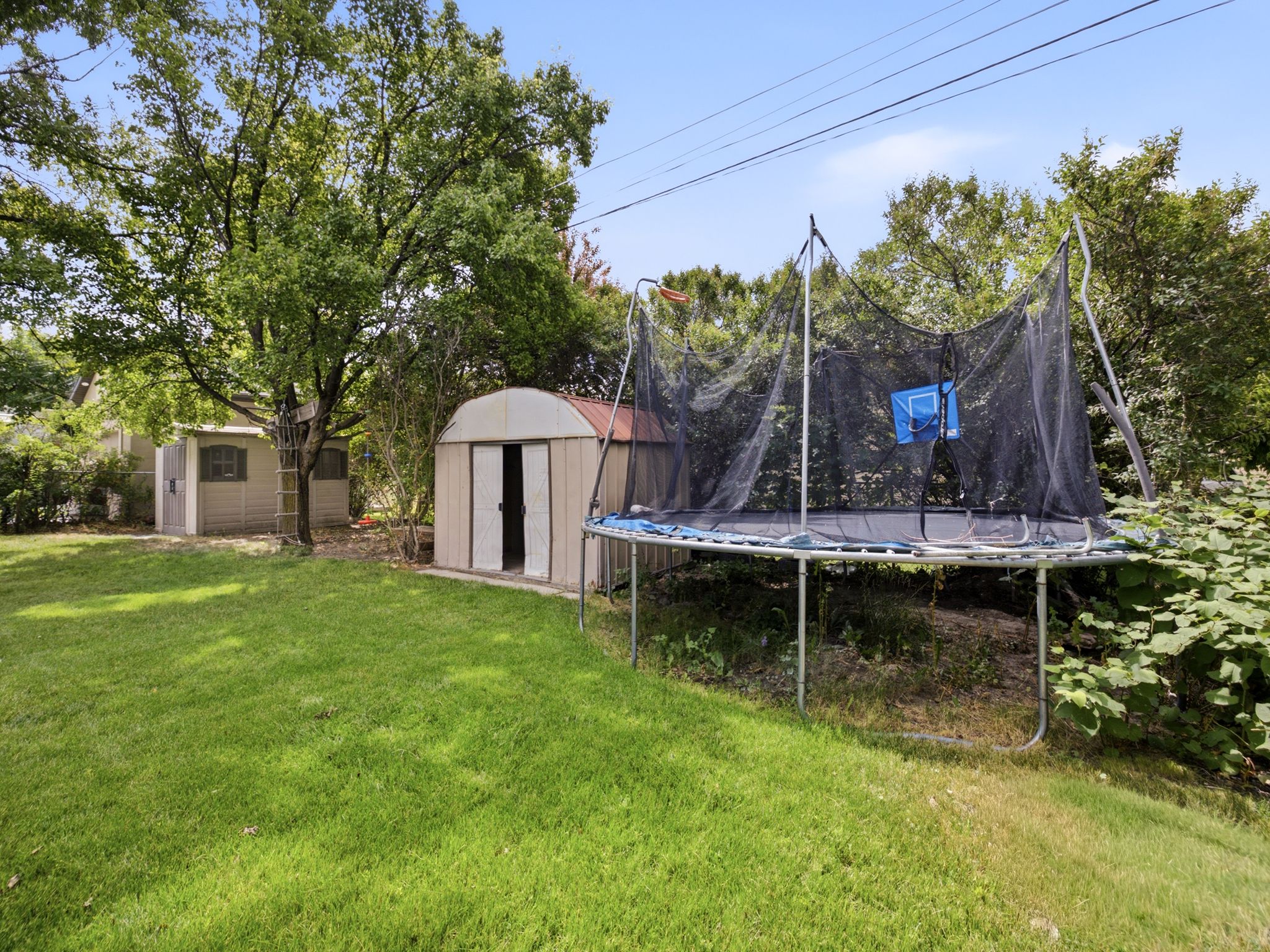 Expansive backyard featuring a lush lawn, mature trees, two storage sheds, and partial fencing