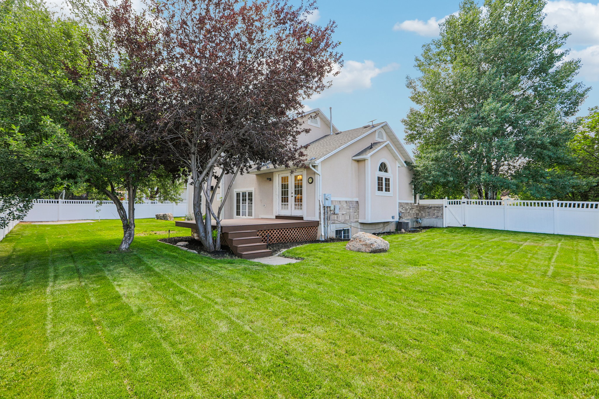 Expansive backyard with a manicured lawn, a multi-tiered deck, mature trees, and a white picket fence