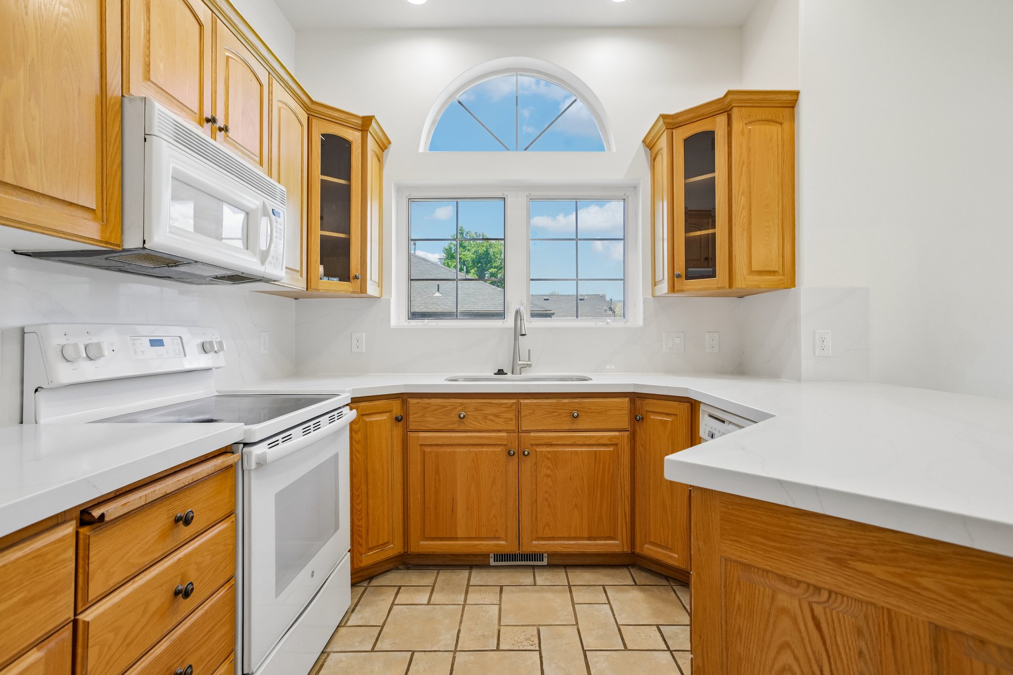 Kitchen featuring wood cabinetry, white countertops, built-in microwave, electric range, and a window with an arched transom