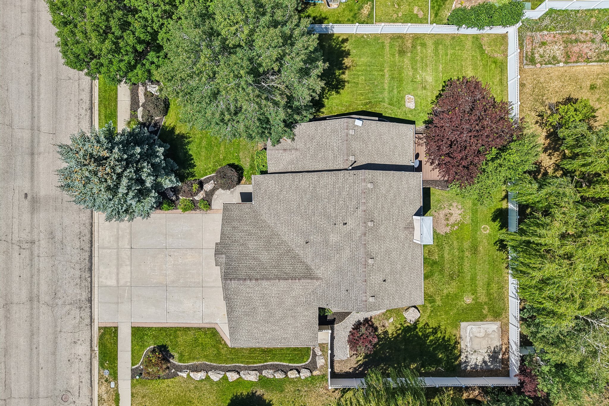 Expansive property featuring a shingled roof, extensive green lawns, mature trees, a multi-car driveway, and perimeter fencing