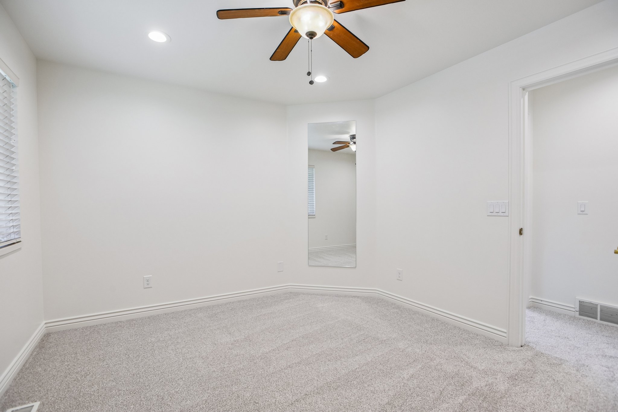 Carpeted room featuring white walls, a ceiling fan with light fixture, recessed lighting, and a full-length wall mirror