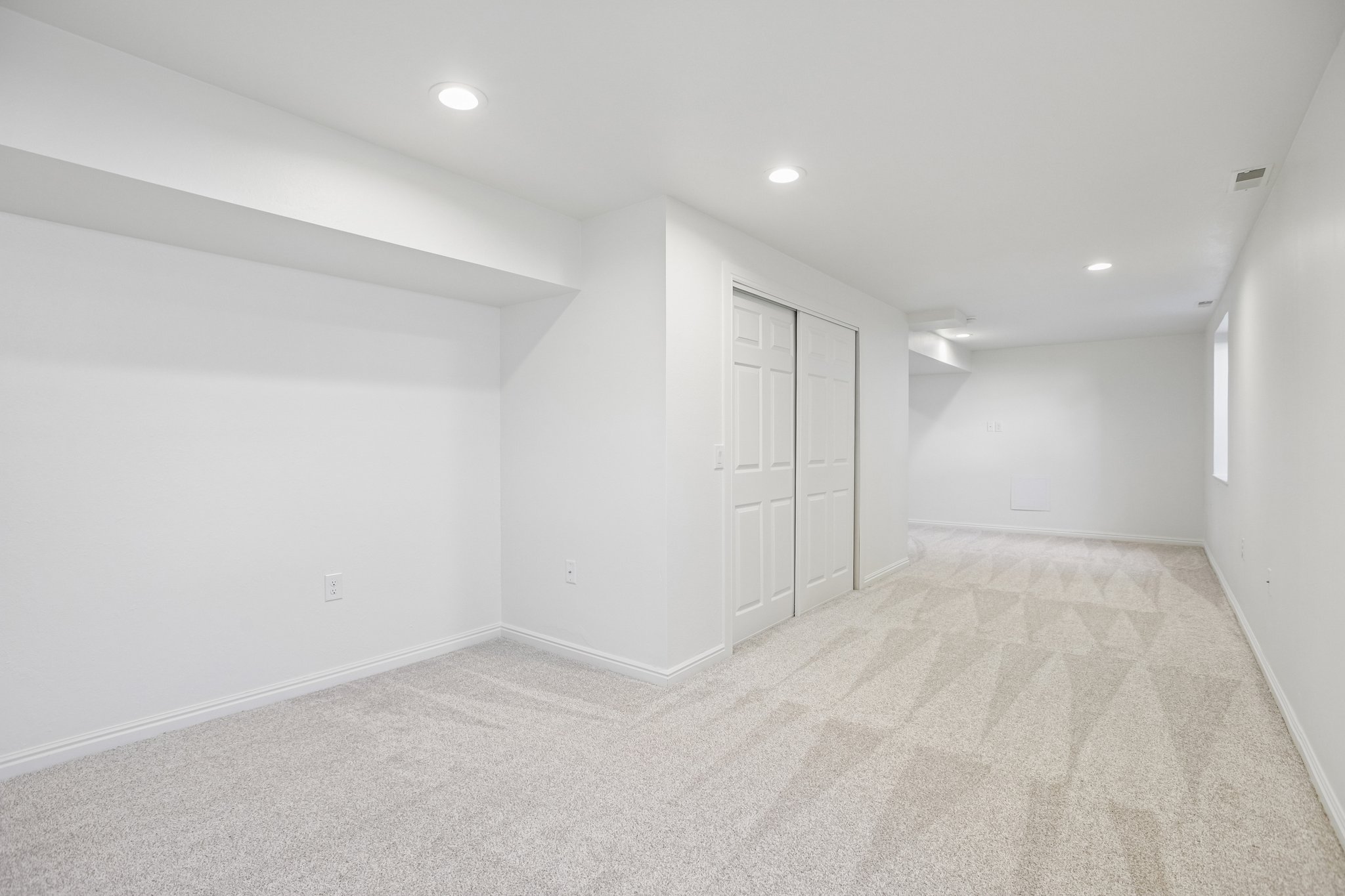 Spacious room featuring light-colored patterned carpeting, white walls, and recessed lighting