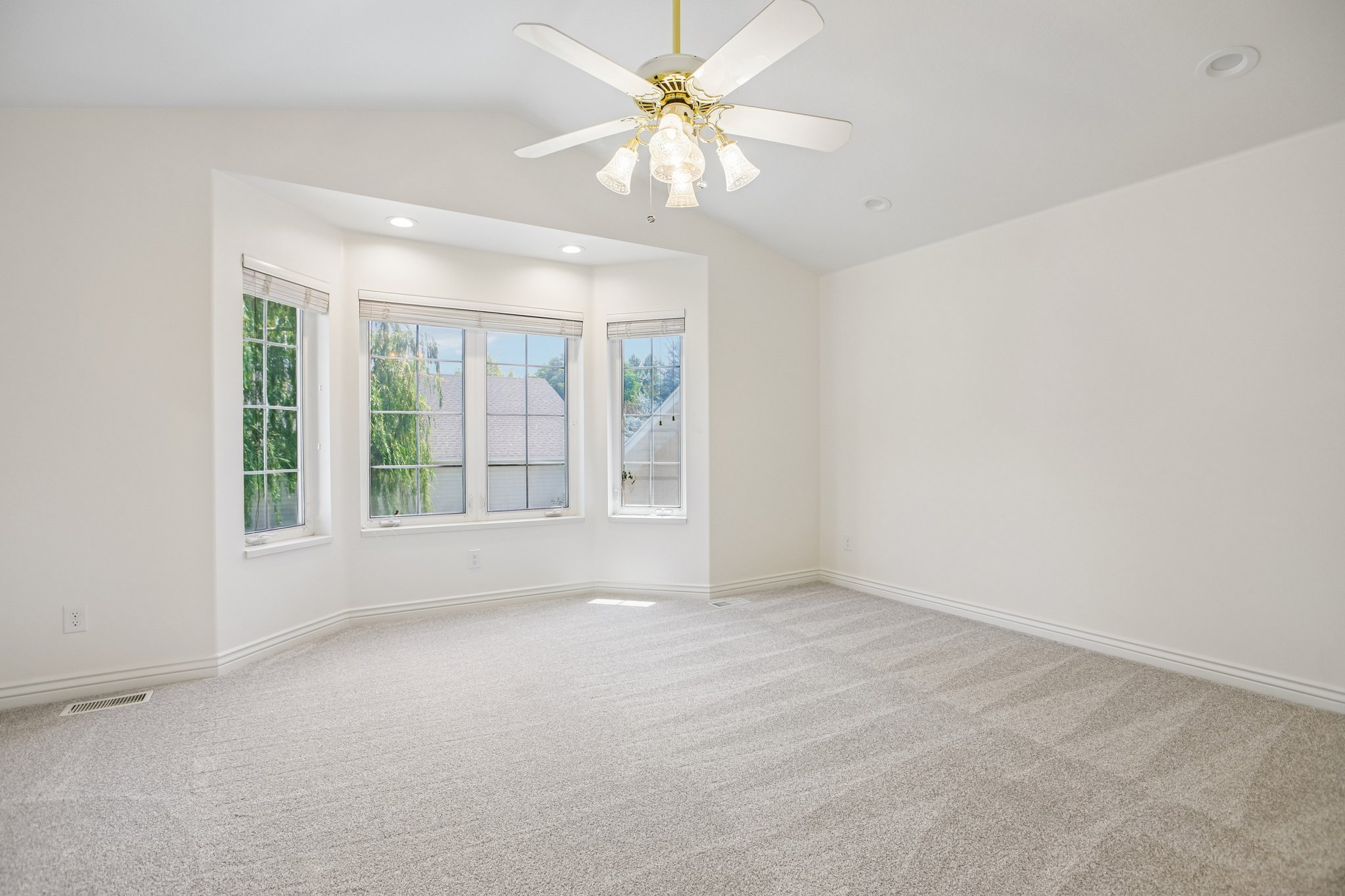 Spacious room featuring light-toned carpeting, a bay window with multiple panes, recessed lighting, and a ceiling fan with integrated light fixture
