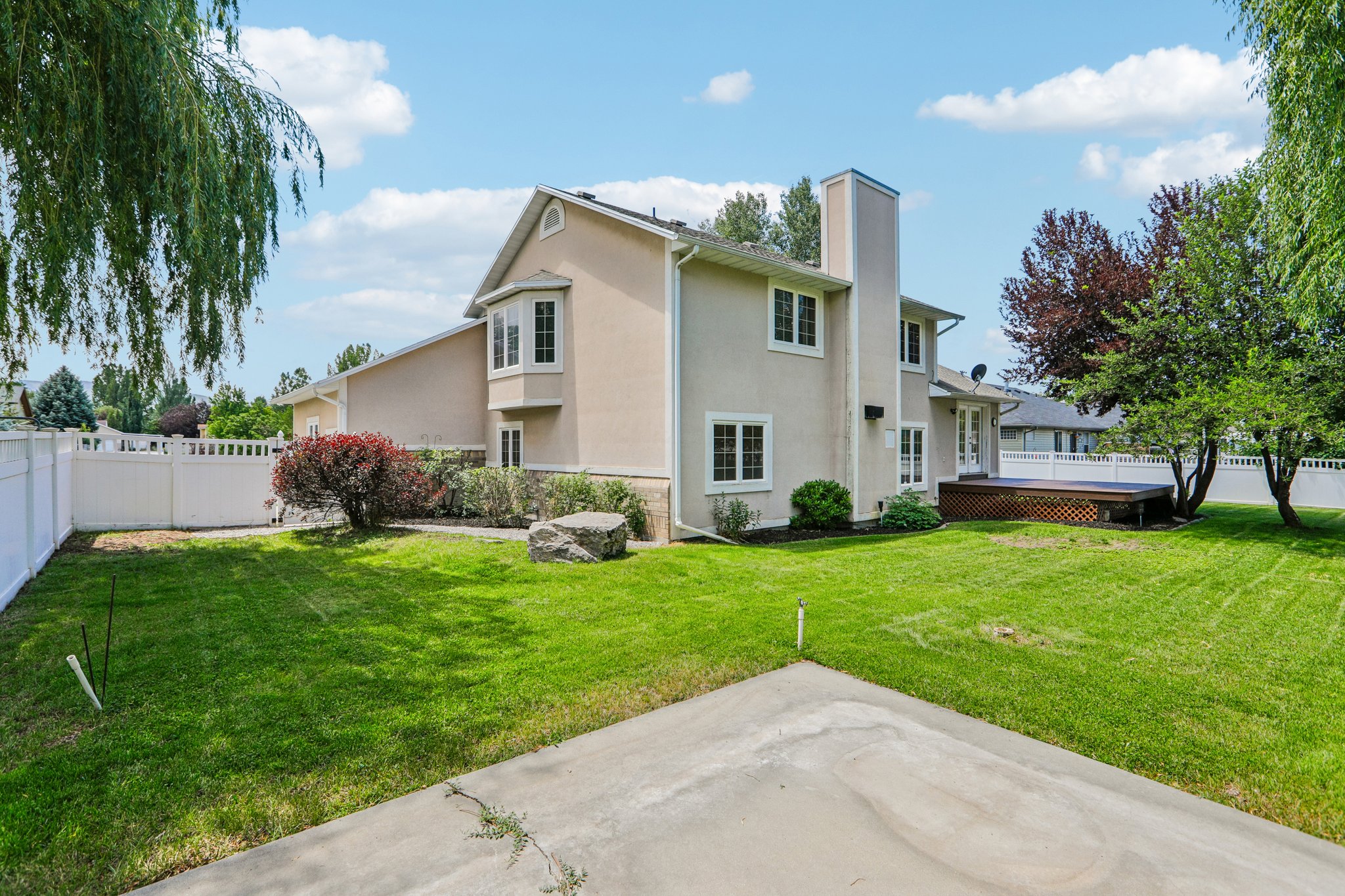 Spacious backyard featuring a stucco exterior, multiple windows, a bay window, a built-in deck, and mature landscaping