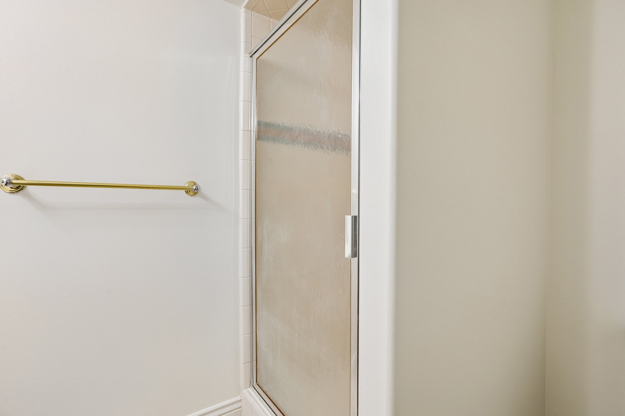 Shower enclosure with a frosted glass door and white frame, accompanied by a brass-finish towel bar