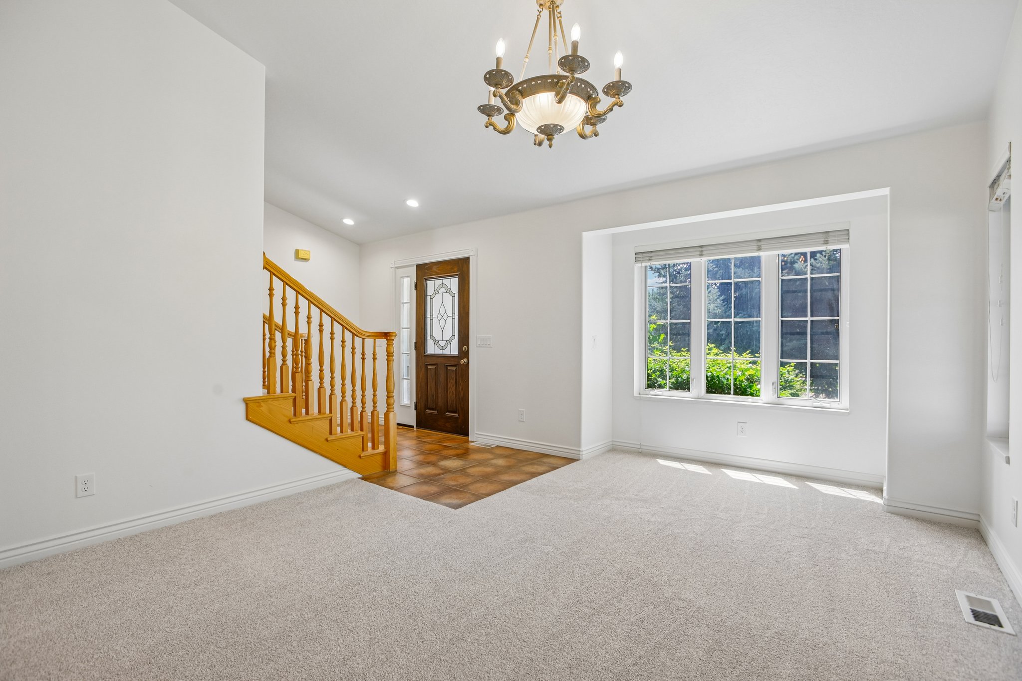 Front entry foyer featuring a dark wood door with decorative glass, a natural wood staircase with a baluster railing, a multi-pane bay window, and a chandelier with glass shades