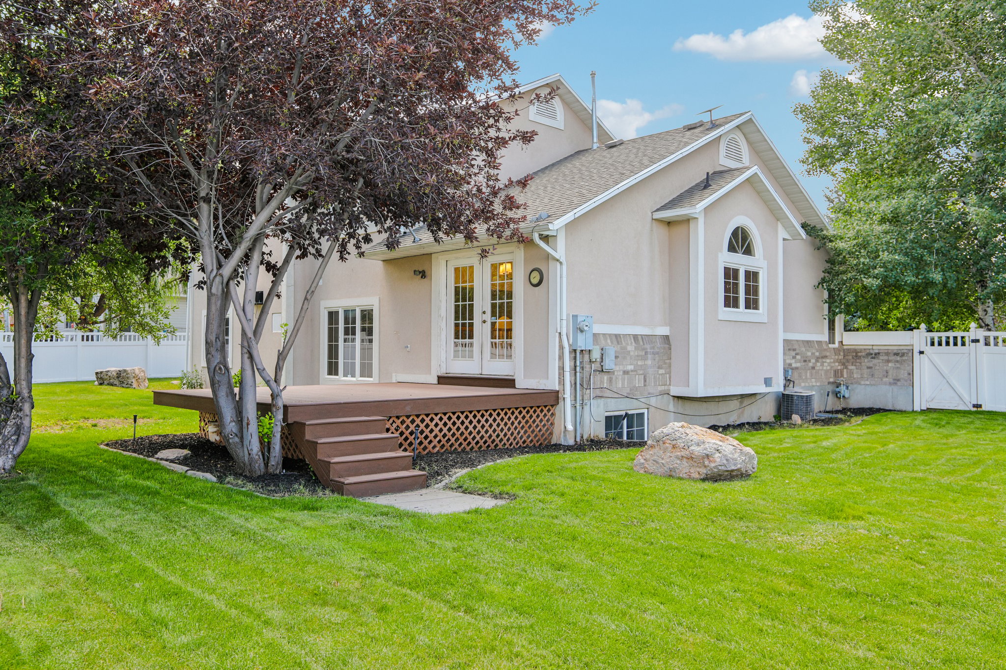 Rear exterior featuring a brown multi-level deck with lattice skirting, stone accent siding, and multiple windows