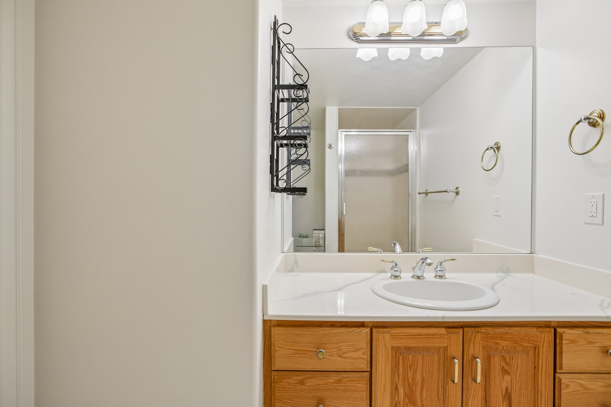 Bathroom vanity featuring a light wood-finish cabinet with brass hardware, a white countertop, and an oval undermount sink with chrome-finish faucet