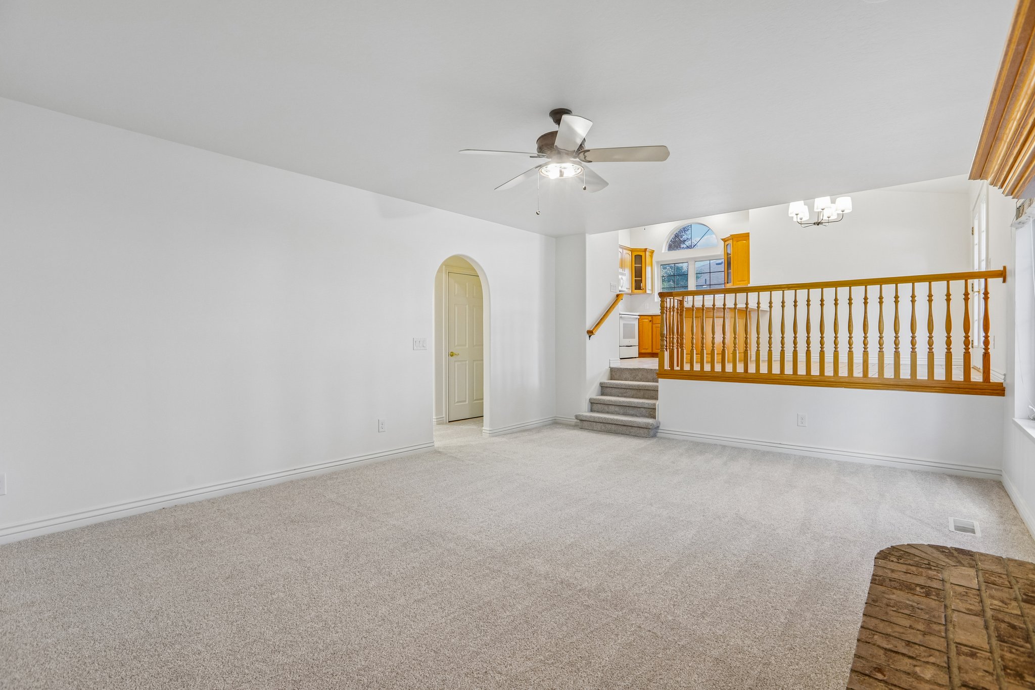 Expansive living area featuring light gray carpeting, crisp white walls, and an arched doorway