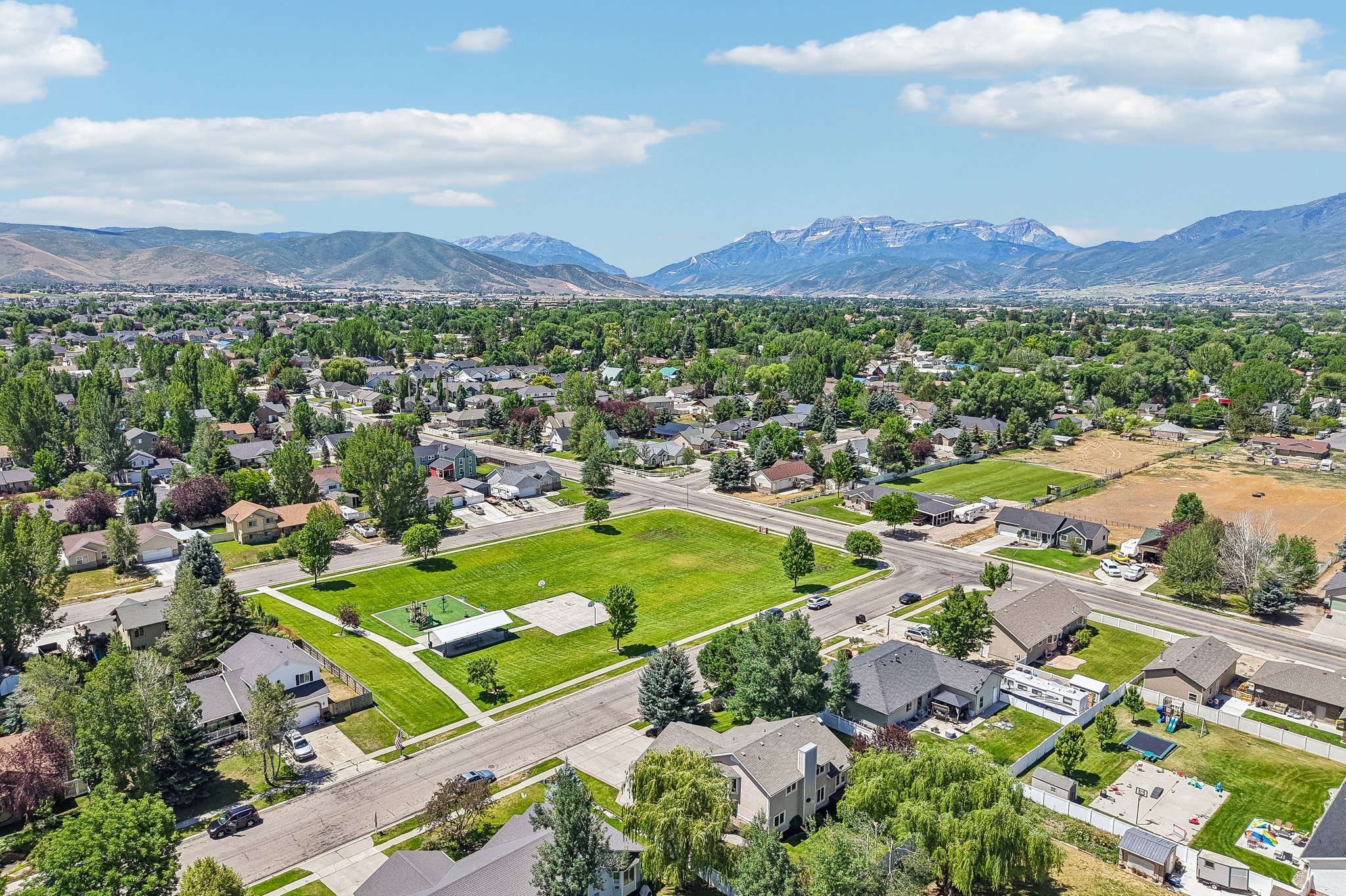 Expansive community with varied residential architecture surrounded by mature trees, a central green space, and distant mountains