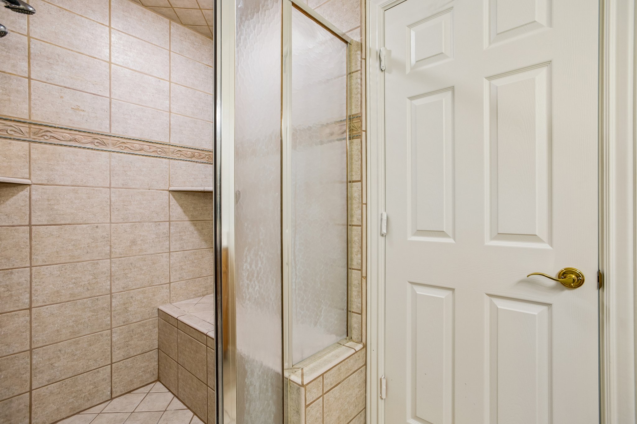 Tiled shower enclosure featuring a built-in bench, decorative accent tile, two recessed shelves, and a glass-paneled door