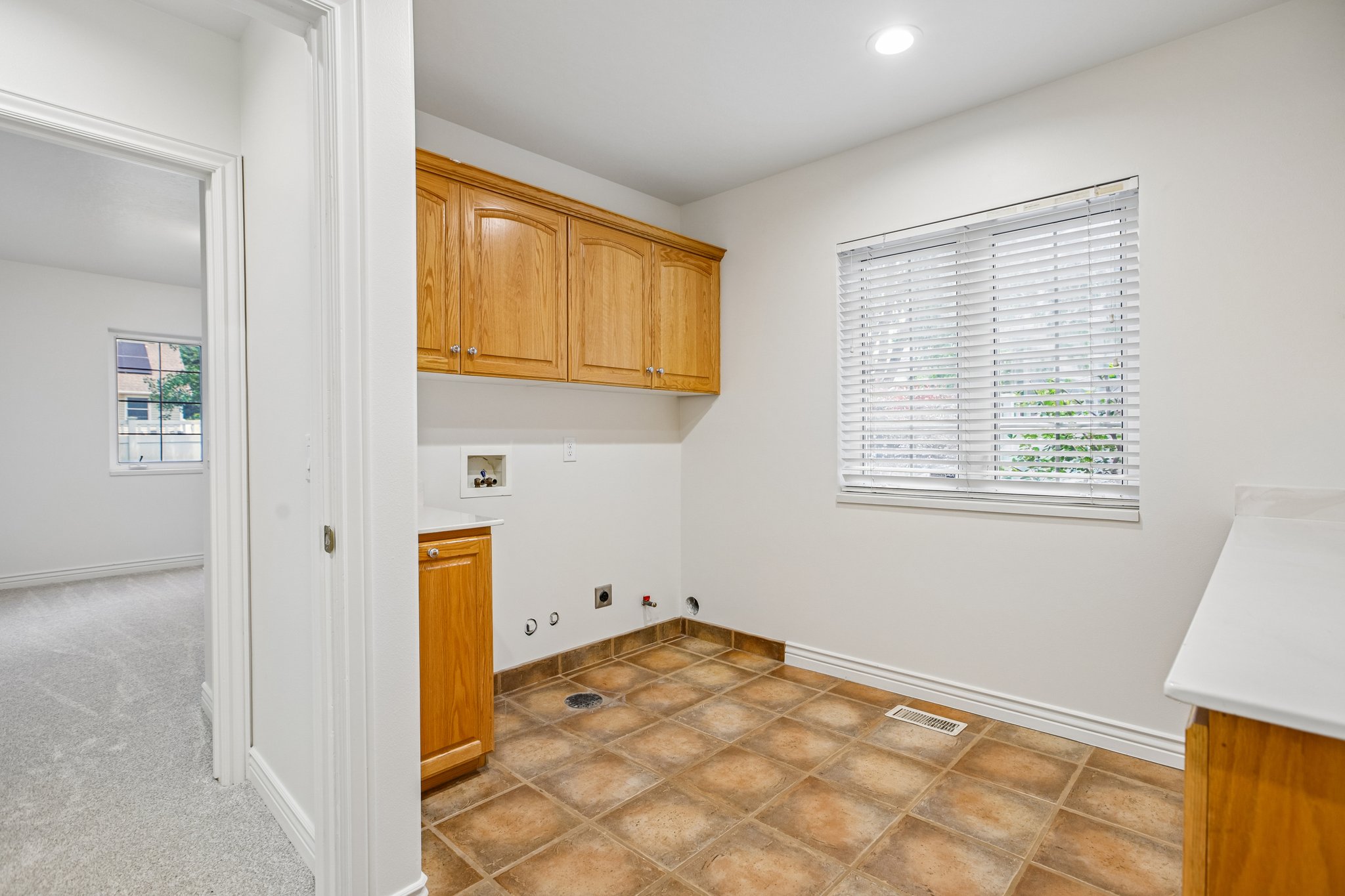 Utility room featuring tile flooring, wood cabinetry, a window with blinds, recessed lighting, and a countertop