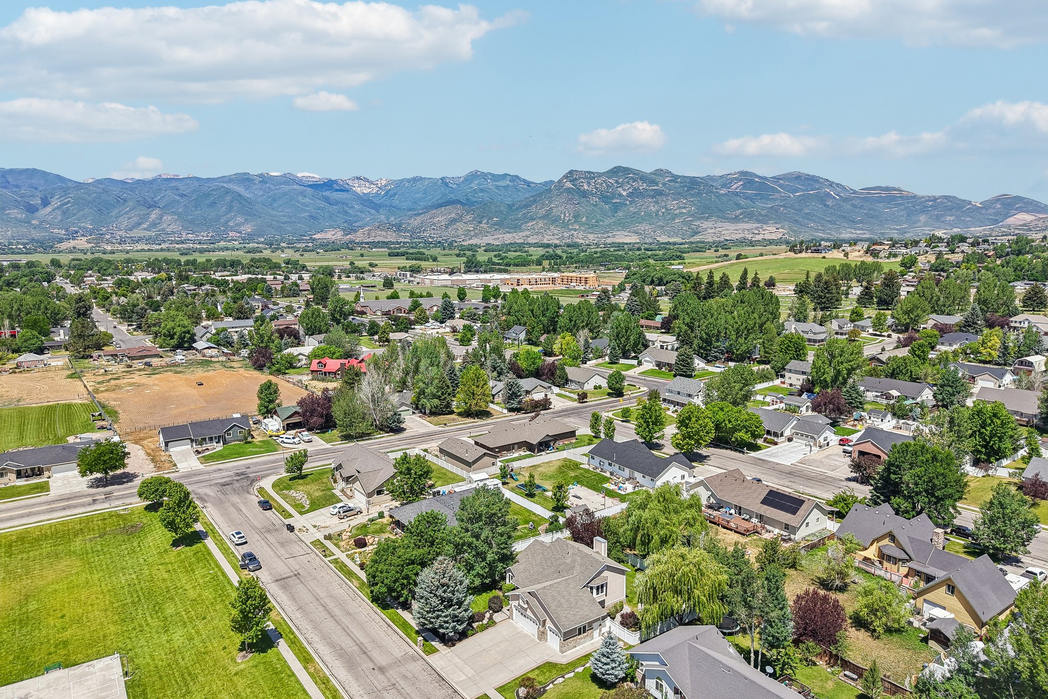 Residential neighborhood featuring detached homes on tree-lined streets, surrounded by green fields and distant mountains