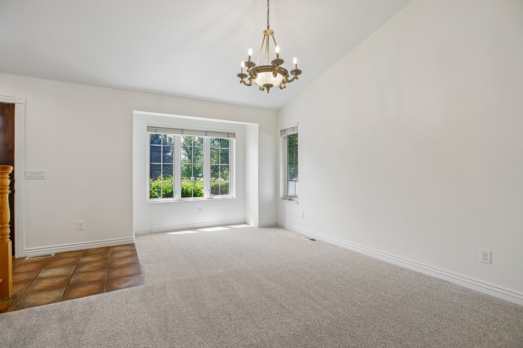 Spacious interior with vaulted ceilings, a prominent bay window, and a decorative chandelier