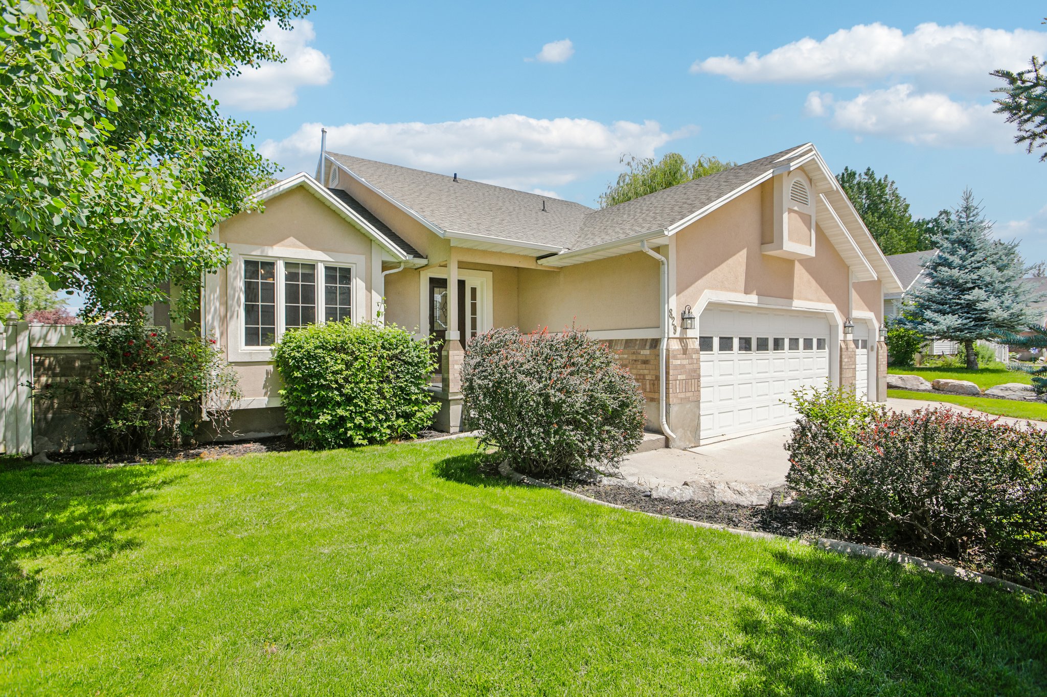 Exterior featuring a light stucco finish, stone veneer accents, multi-pane windows, an attached two-car garage, and established landscaping