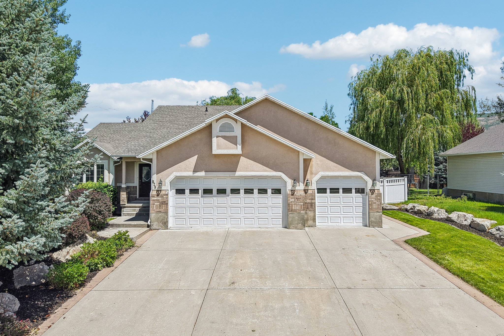 Exterior featuring a three-car garage, stone accents, and a stucco finish