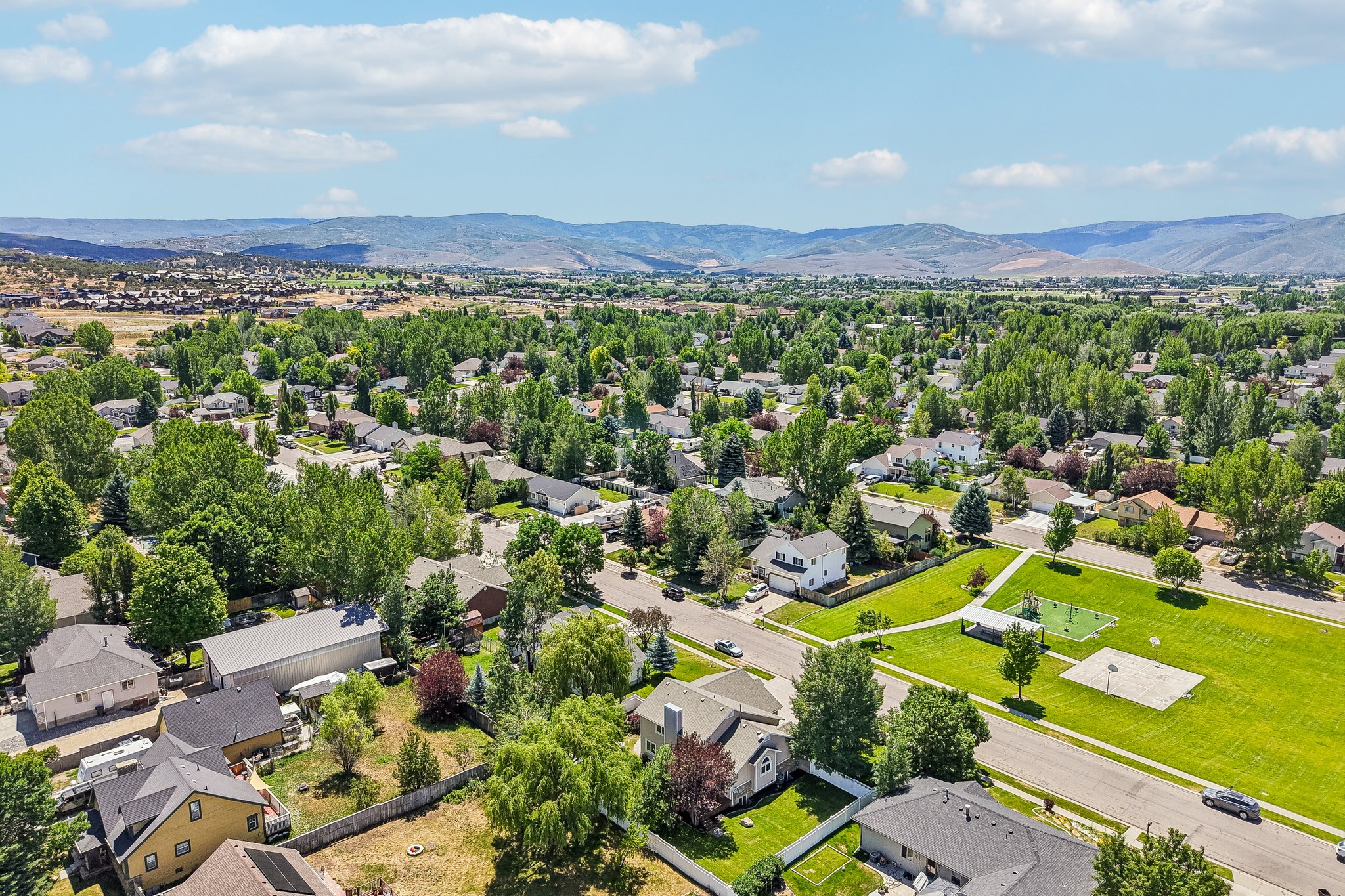 Expansive residential area featuring established homes, mature trees, open green spaces, and mountain backdrops