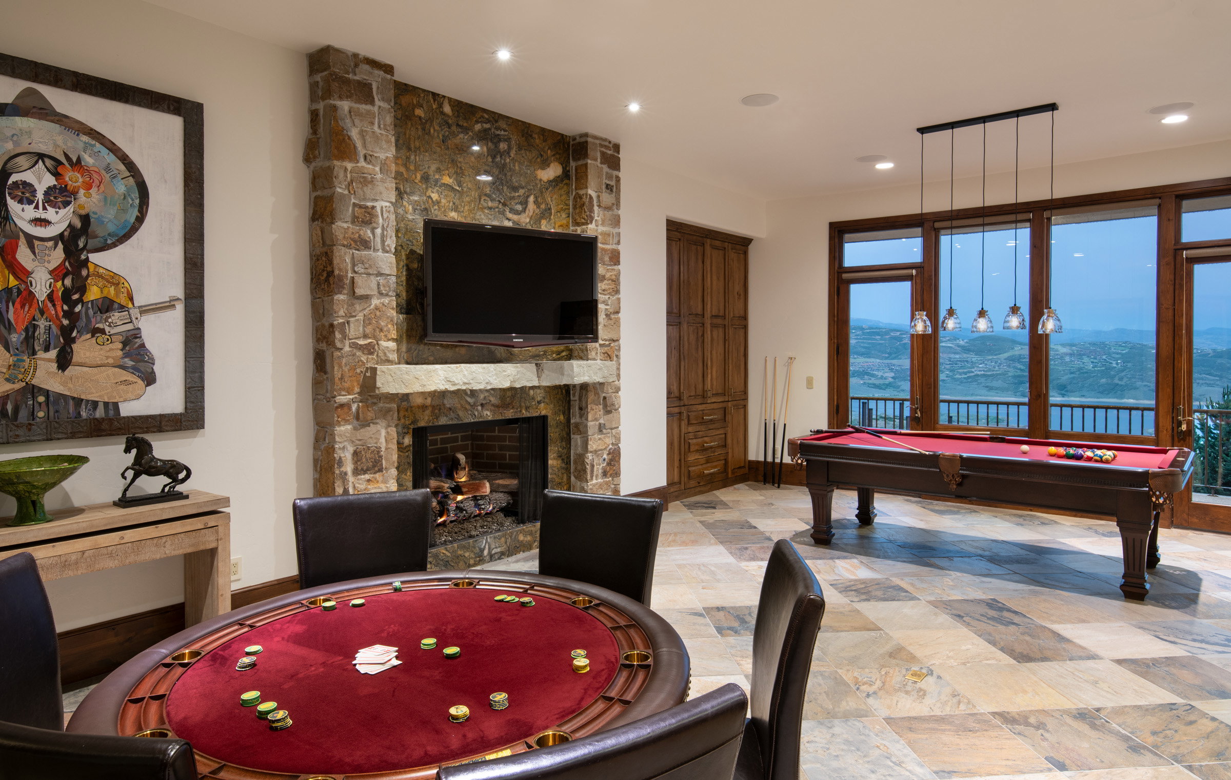 Expansive recreation room featuring a stone-clad fireplace and hearth, wood-frame windows, wood-finish flooring, and built-in wood cabinetry