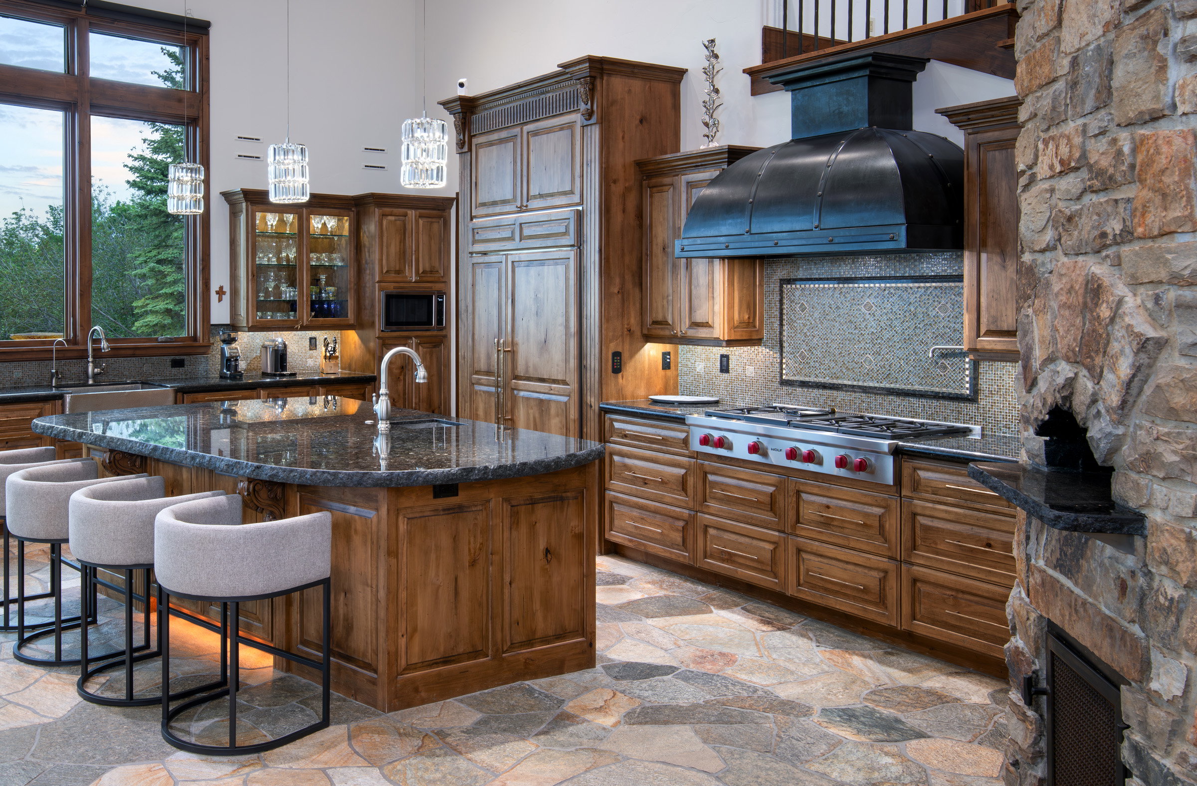 Gourmet kitchen with flagstone flooring, wood cabinetry, stone countertops, and a stone-clad pizza oven
