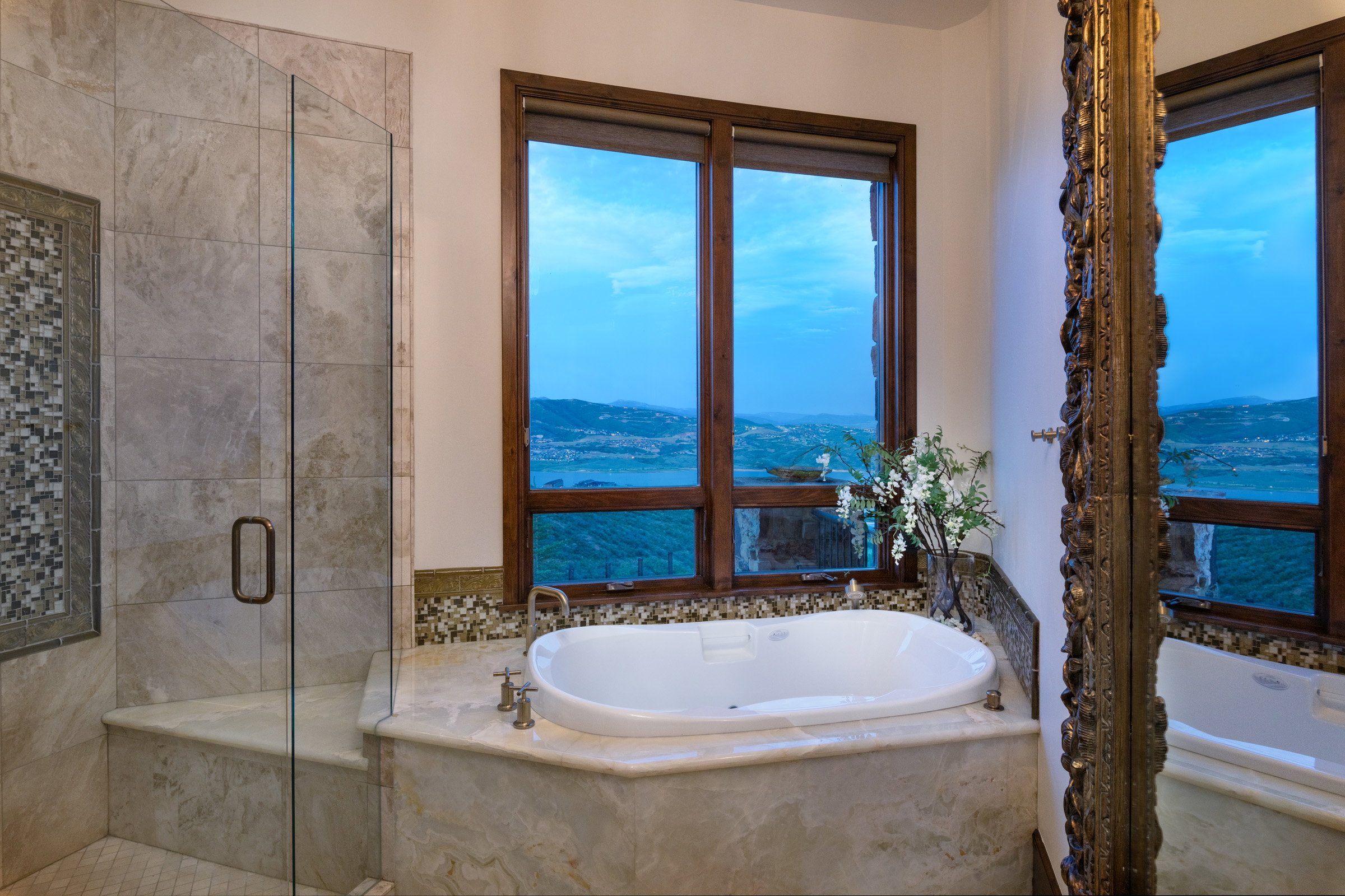 Soaking tub with surrounding marble-finish decking, framed by large windows