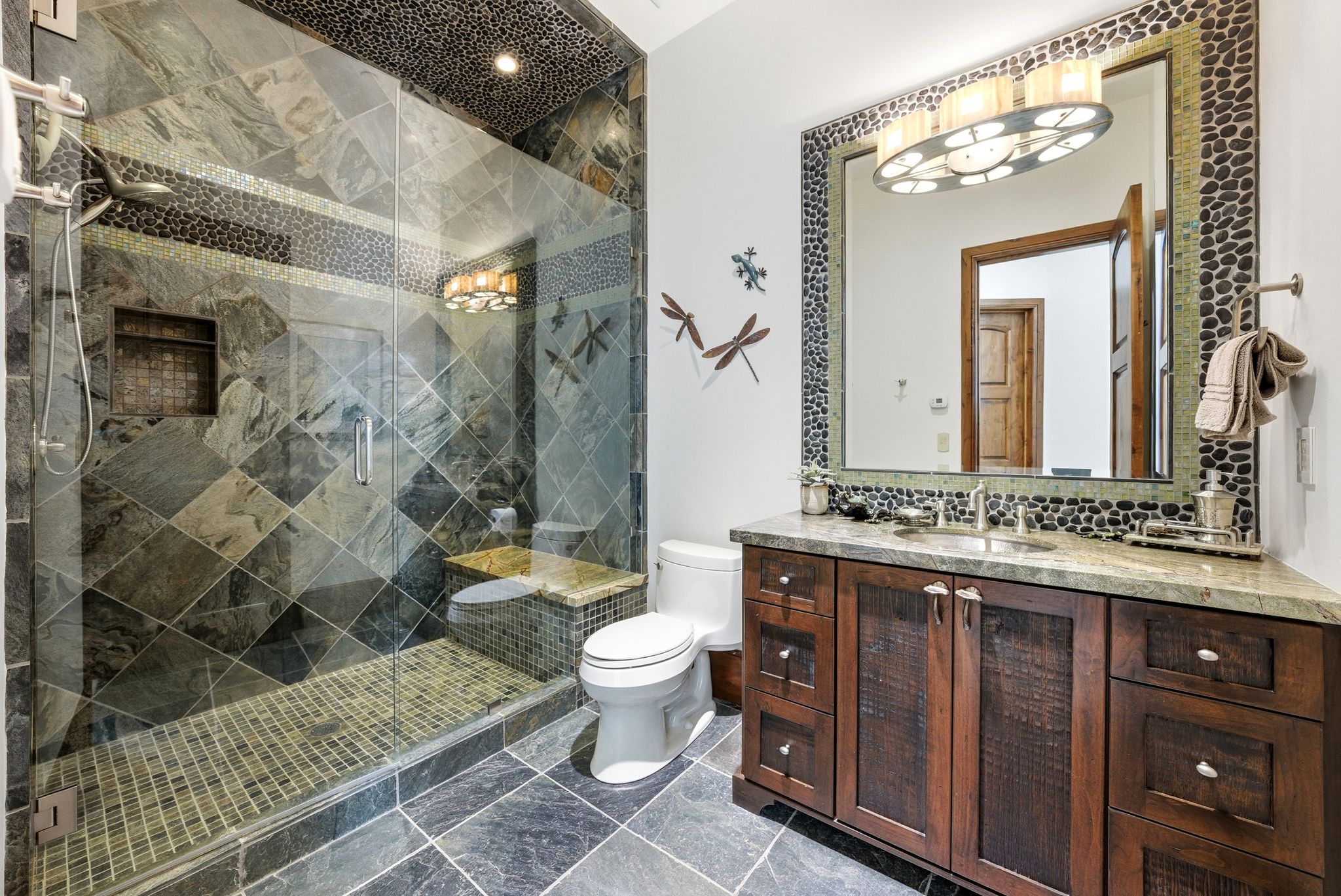 Spacious bathroom featuring a glass-enclosed shower with stone tile walls, a built-in bench, and a tiled shower pan