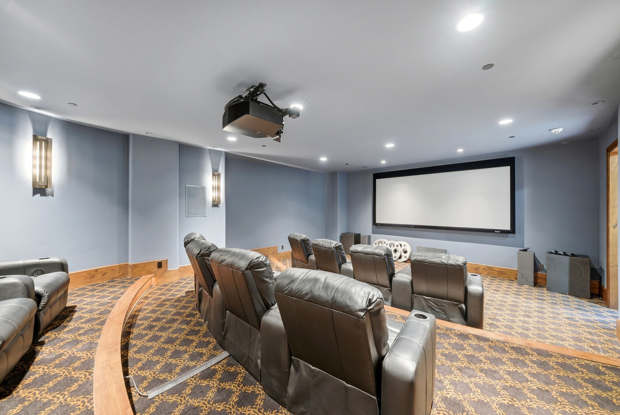 Dedicated home theater featuring a large projection screen, ceiling-mounted projector, patterned carpeting, and recessed lighting