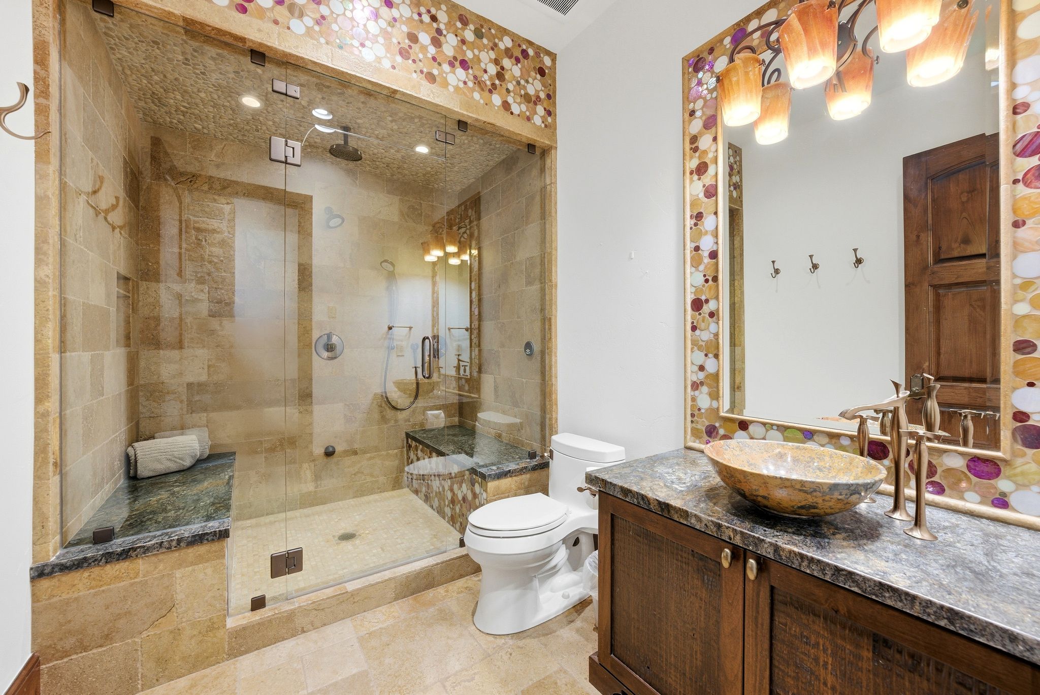 Spacious bathroom featuring a glass-enclosed shower with stone tile, a built-in shower bench, and a rain shower head