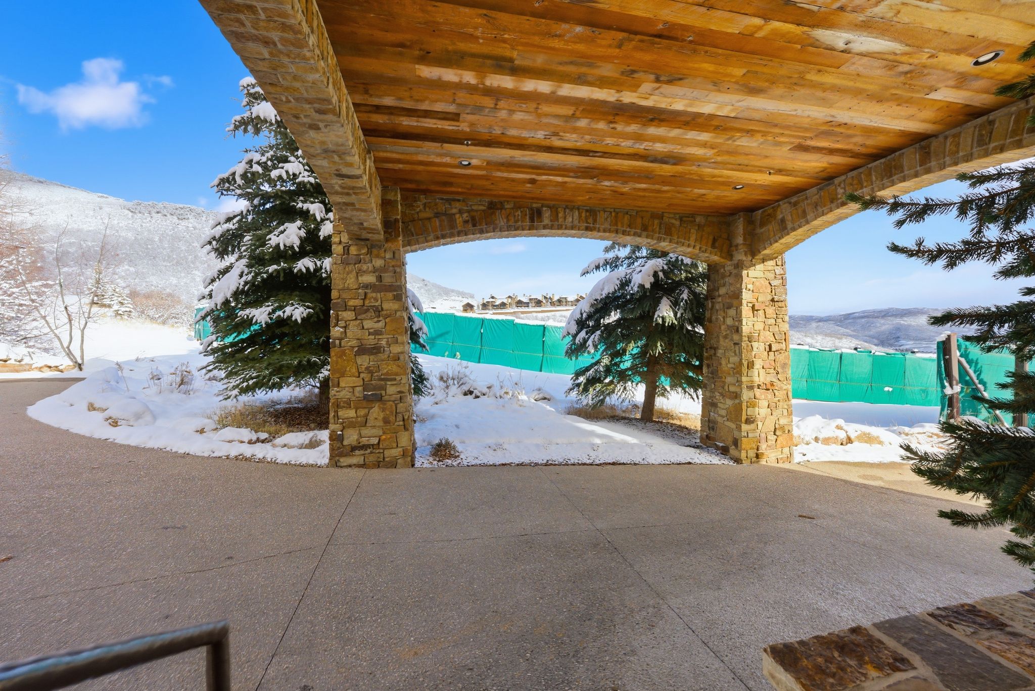 Stone archway entry featuring a wood-finish ceiling with recessed lighting, exposed aggregate concrete driveway, and surrounding winter landscaping