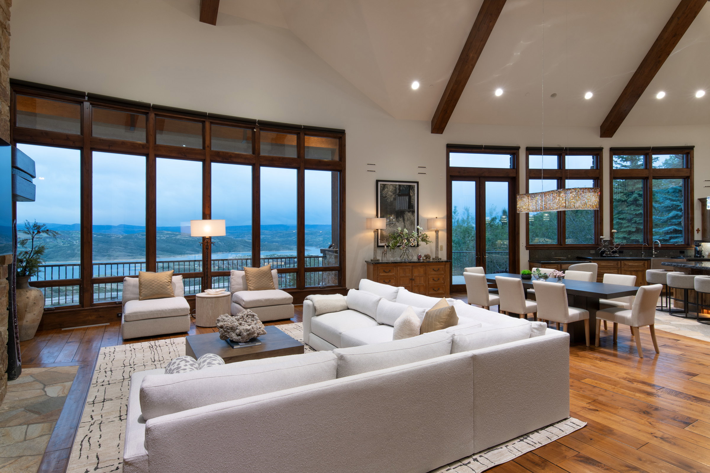 Expansive great room featuring a vaulted ceiling with exposed wood beams, hardwood flooring, and a stone fireplace surround
