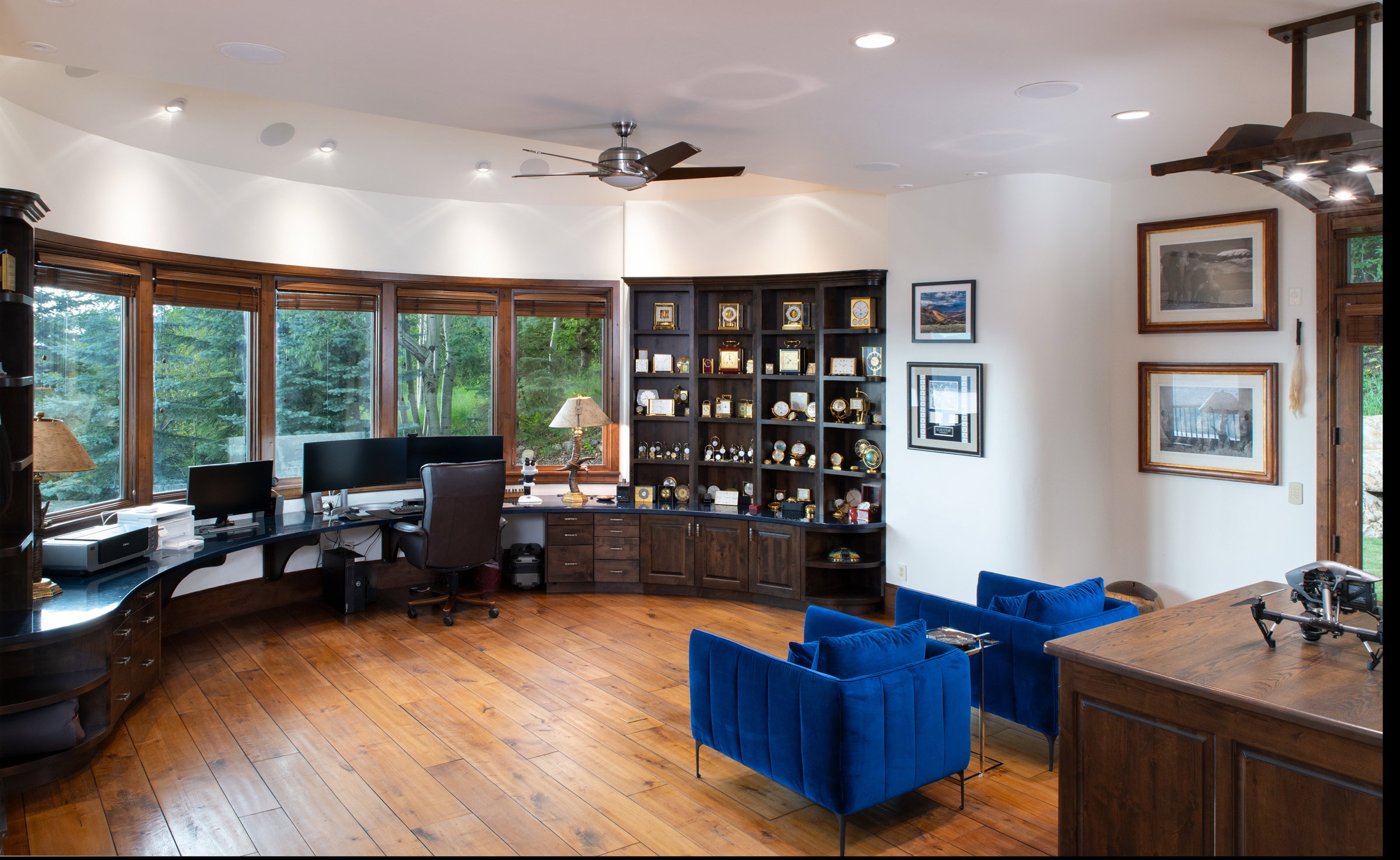 Dedicated office space featuring expansive curved windows, wood-finish flooring, built-in desk cabinetry, recessed lighting, and a ceiling fan