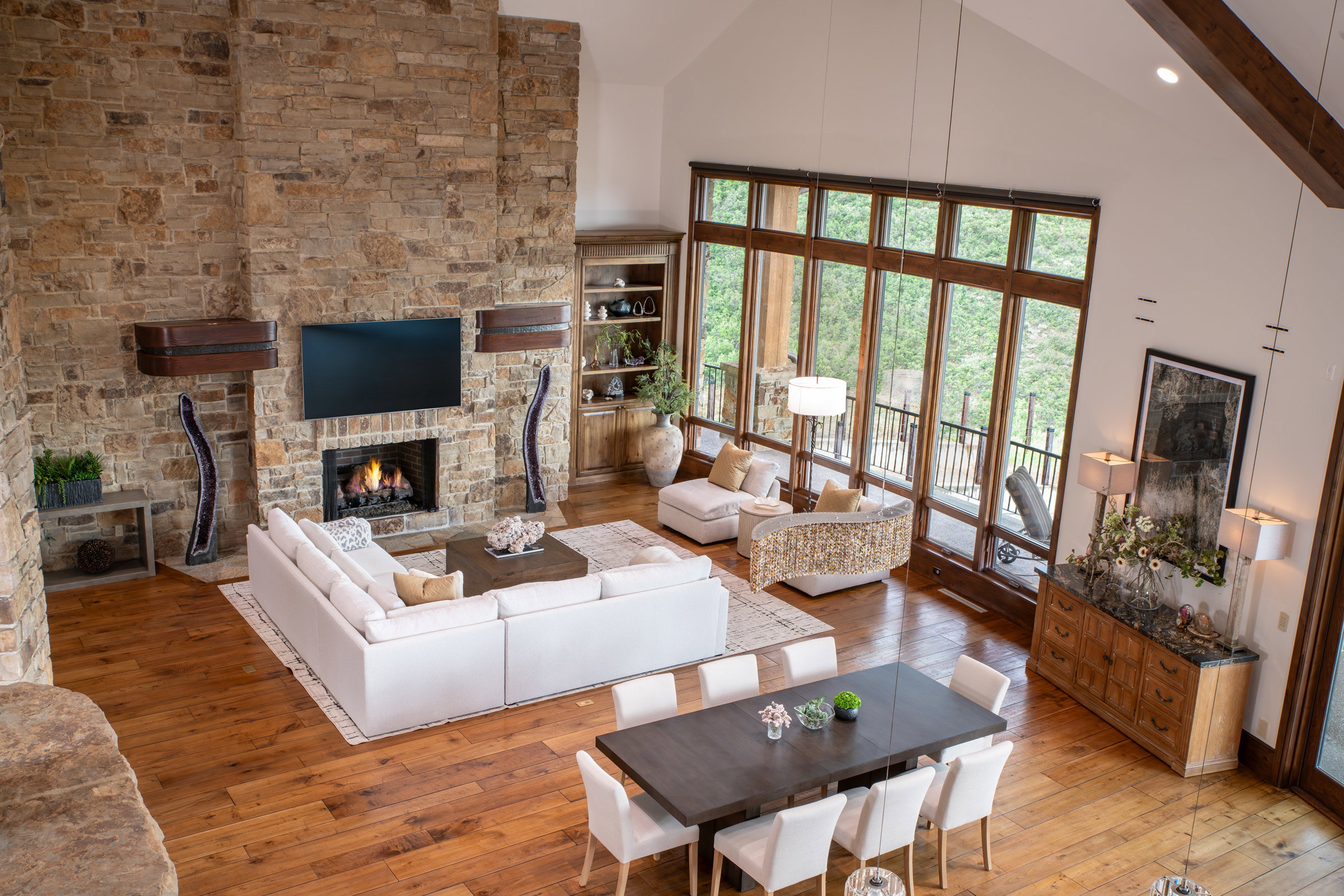 Great room featuring a vaulted ceiling with exposed beams, a floor-to-ceiling stone fireplace, and expansive wood-frame windows